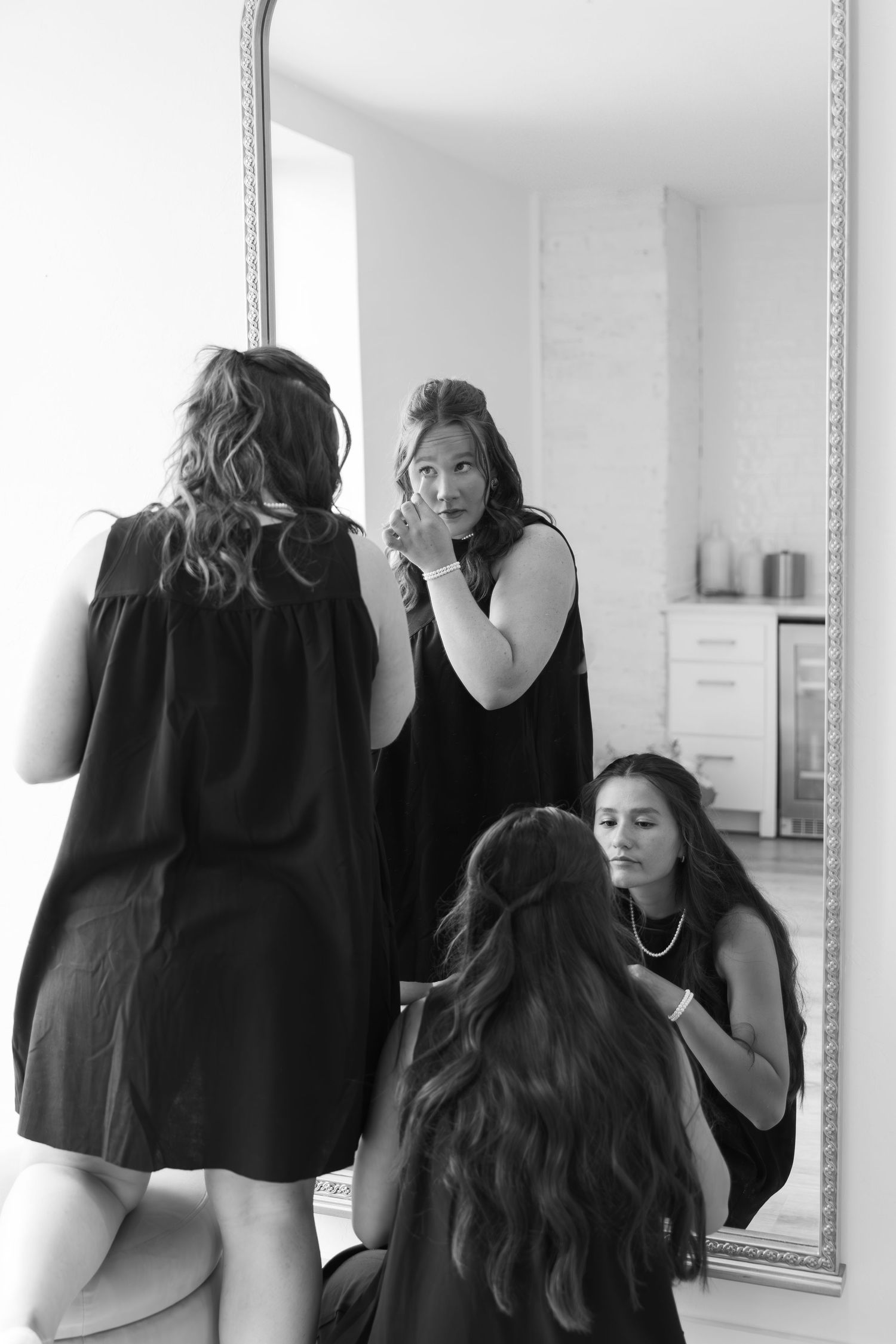 Wedding preparations scene with group in black dresses looking in mirror.
