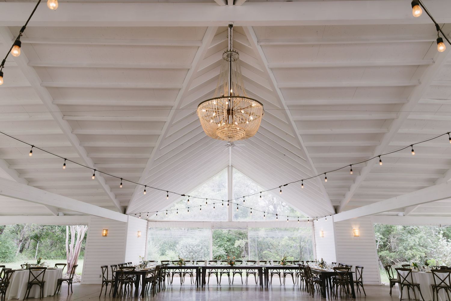 White wedding reception tent interior with elegant chandelier and string lights creating a romantic atmosphere.