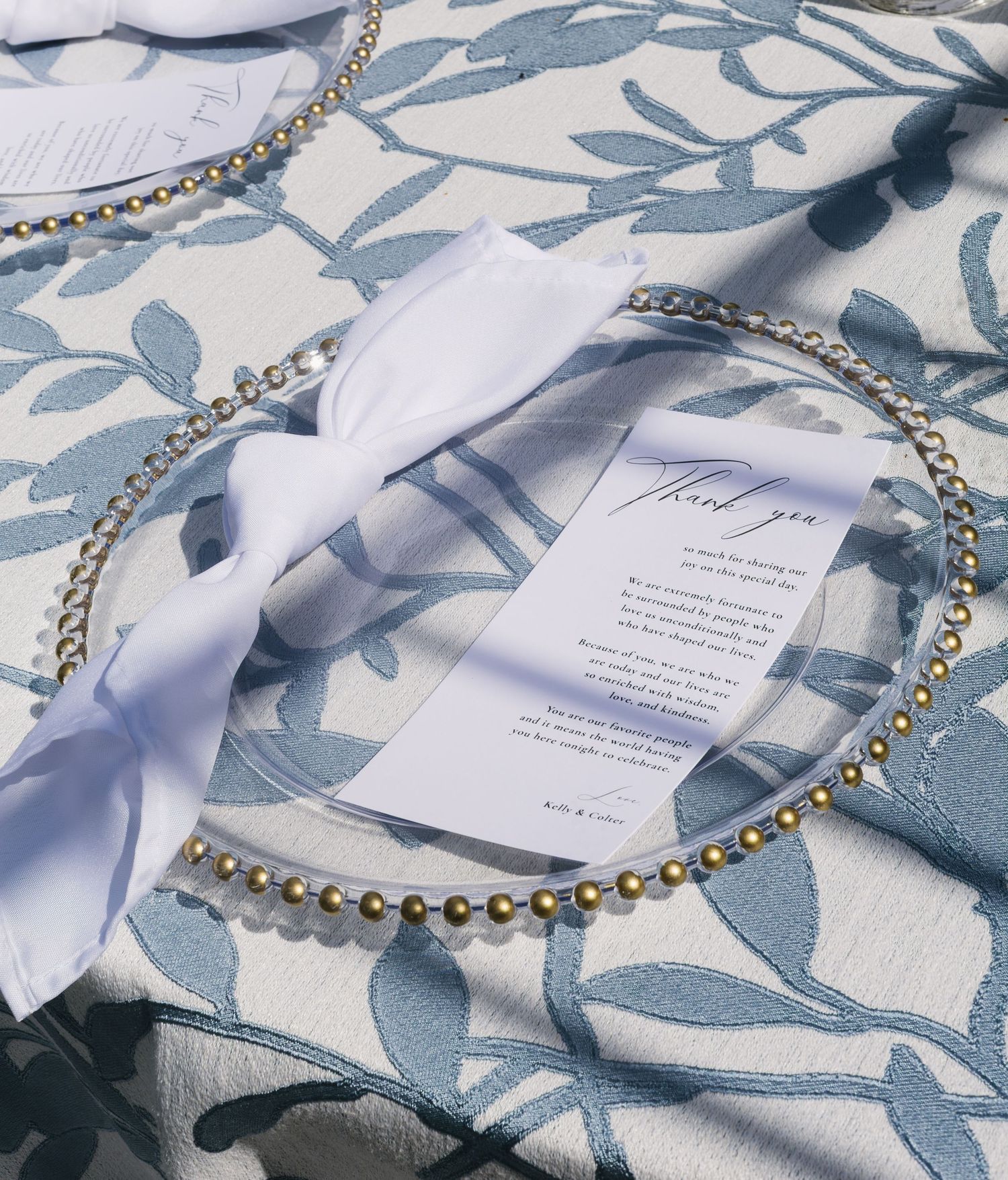 Elegant table setting with white linens, blue floral patterns, and delicate pearl-like beaded necklace decor.