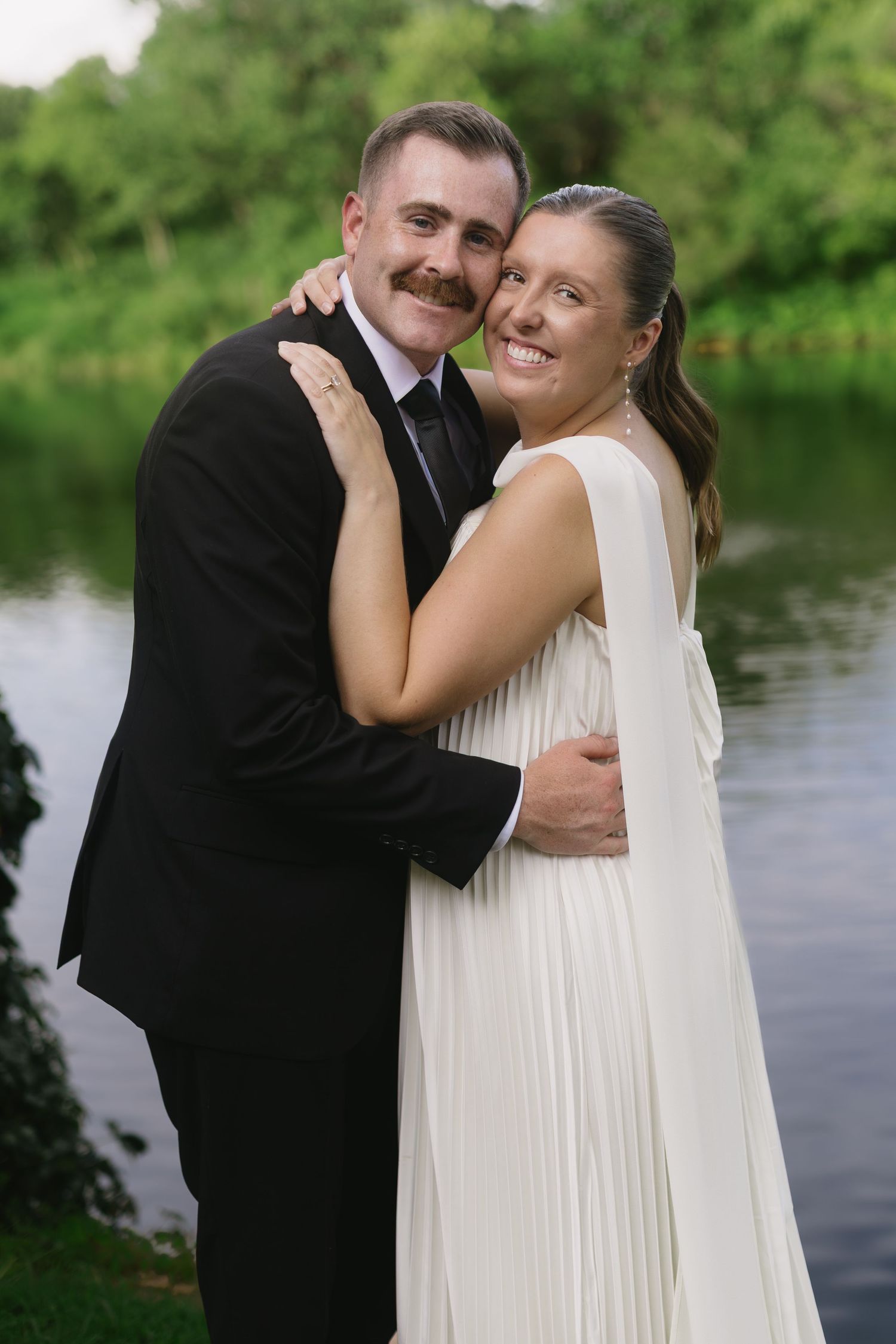 A couple in wedding attire embracing by a lake.