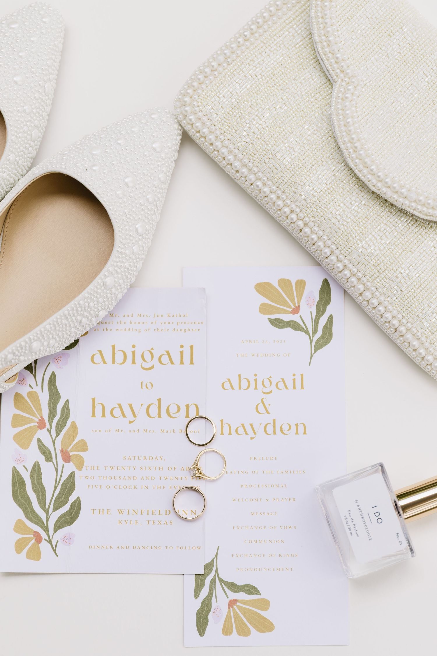 White wedding stationery with gold lettering and floral designs displayed alongside rings and elegant details.