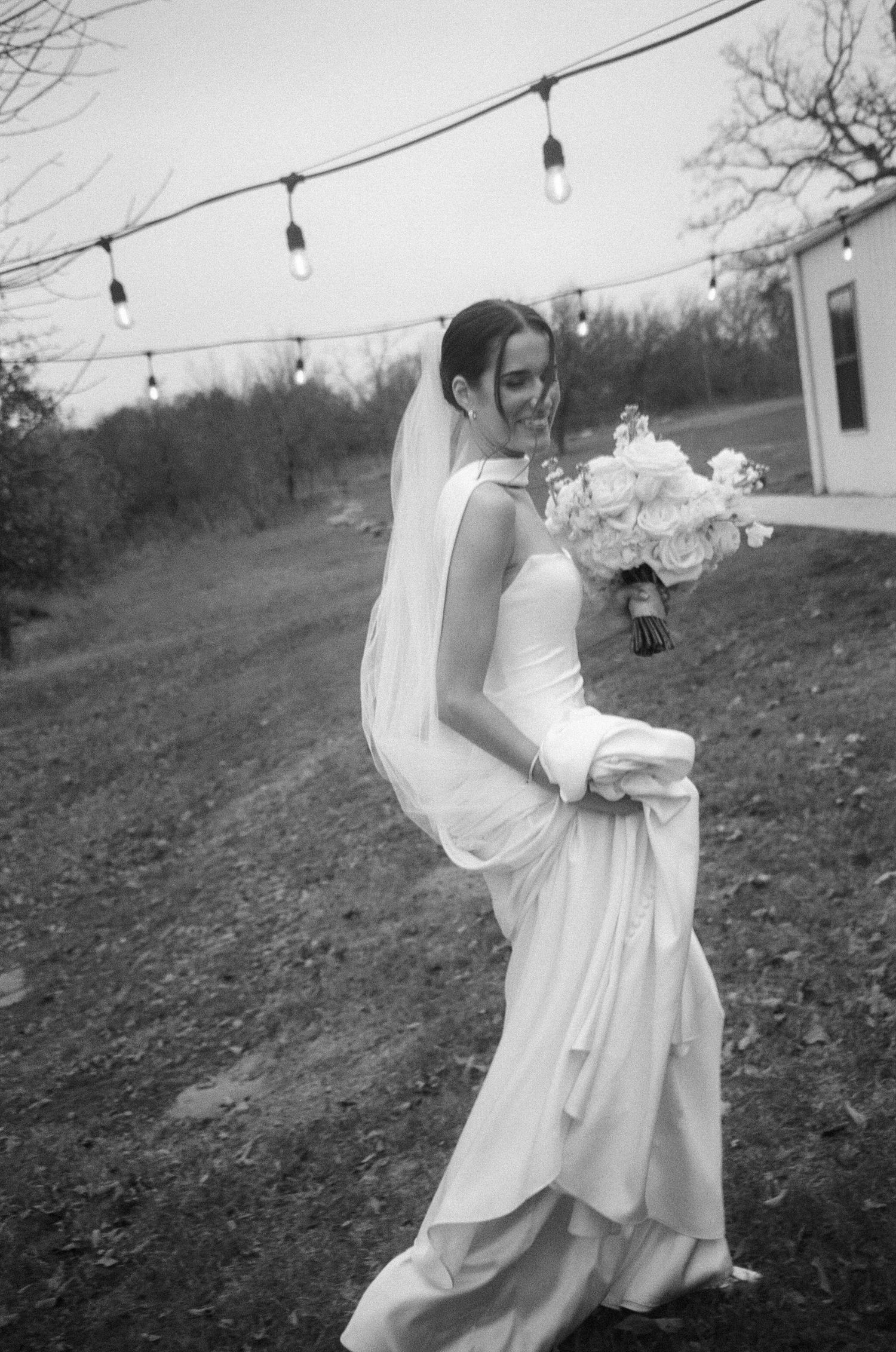 Candid outdoor wedding photos with string lights and flowing white dress in natural setting.