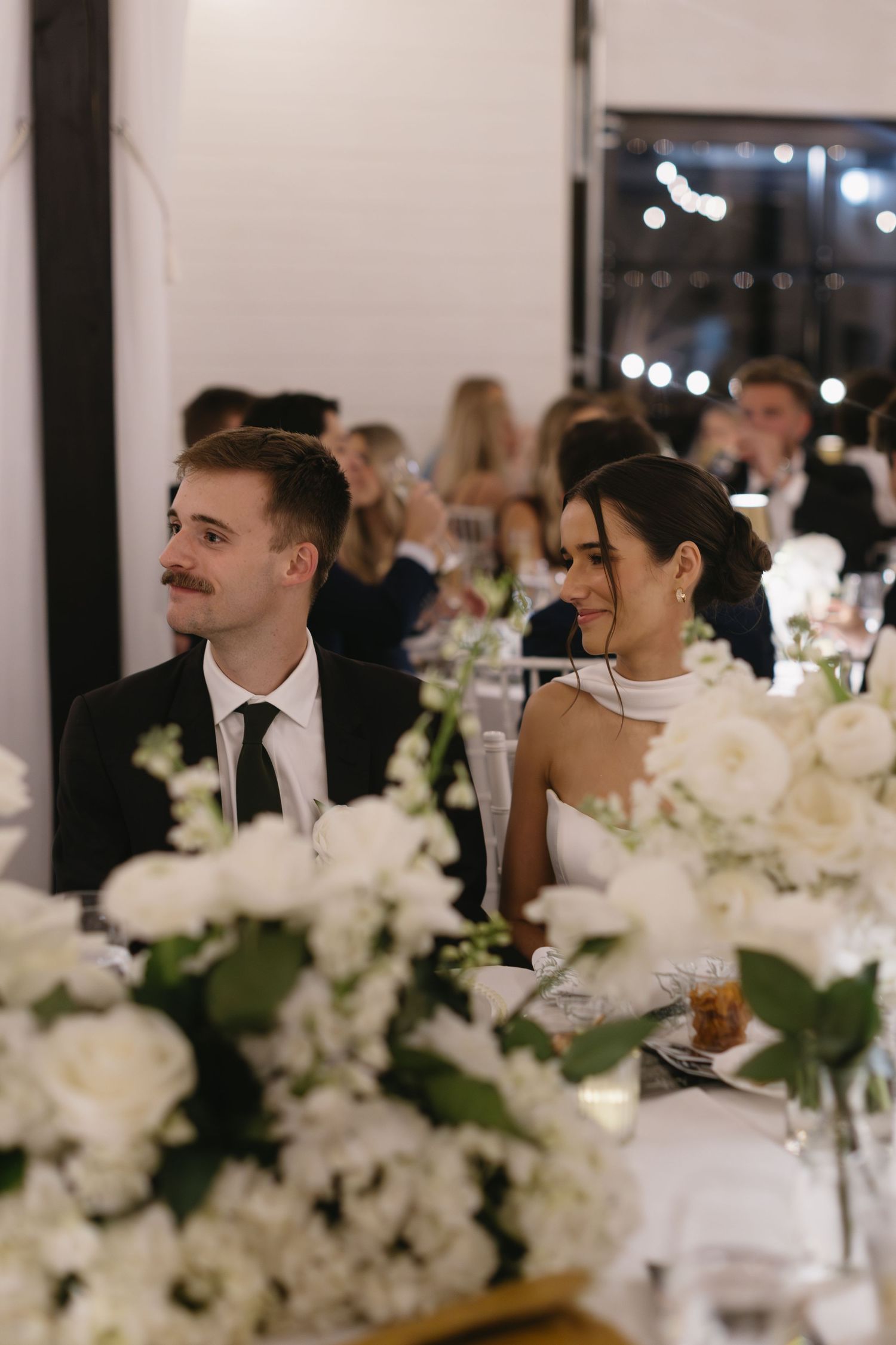 Wedding reception dinner table with elegant white floral centerpieces and ambient lighting.