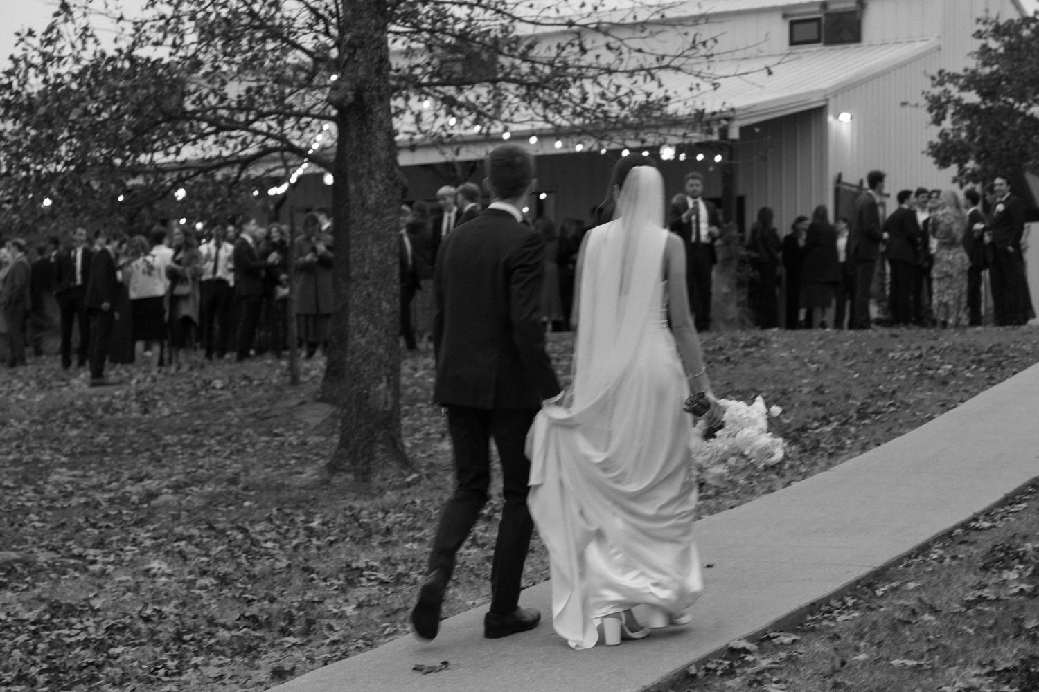 Wedding ceremony guests line a walkway outdoors as a bride in white walks past.