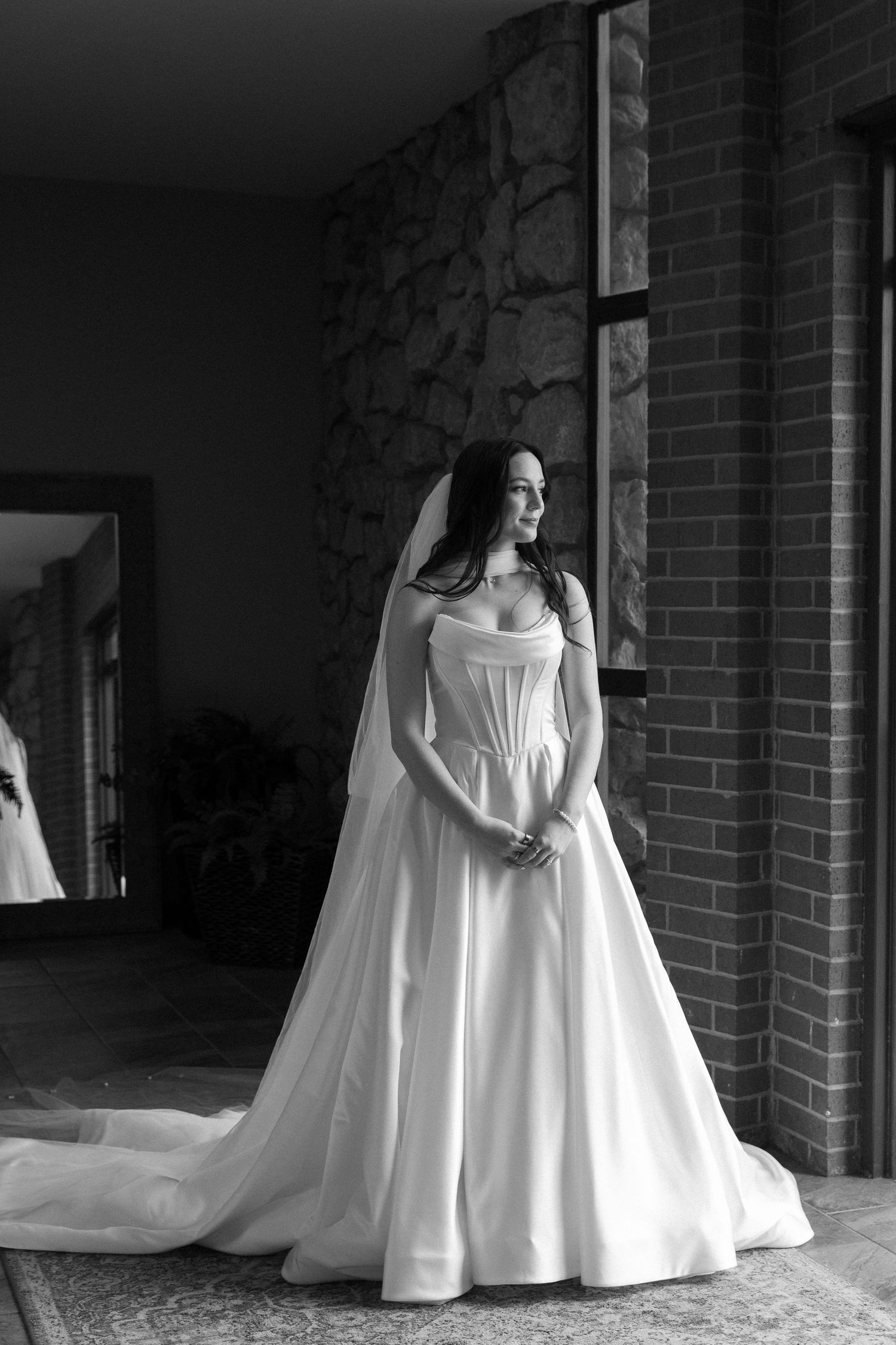 Elegant white wedding dress photographed in dramatic black and white against a brick exterior.