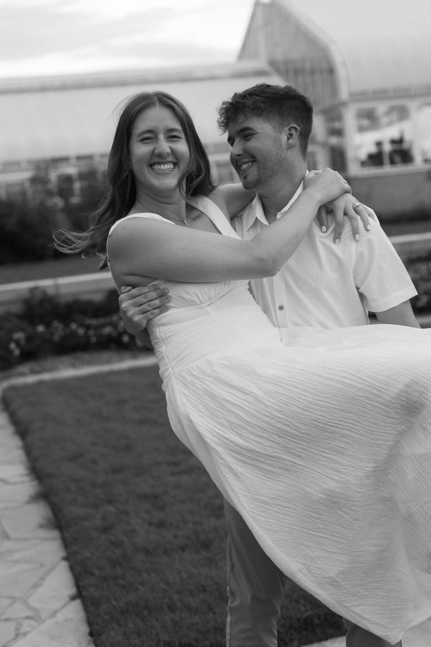 A black and white photo capturing a playful moment as a couple dances outdoors.