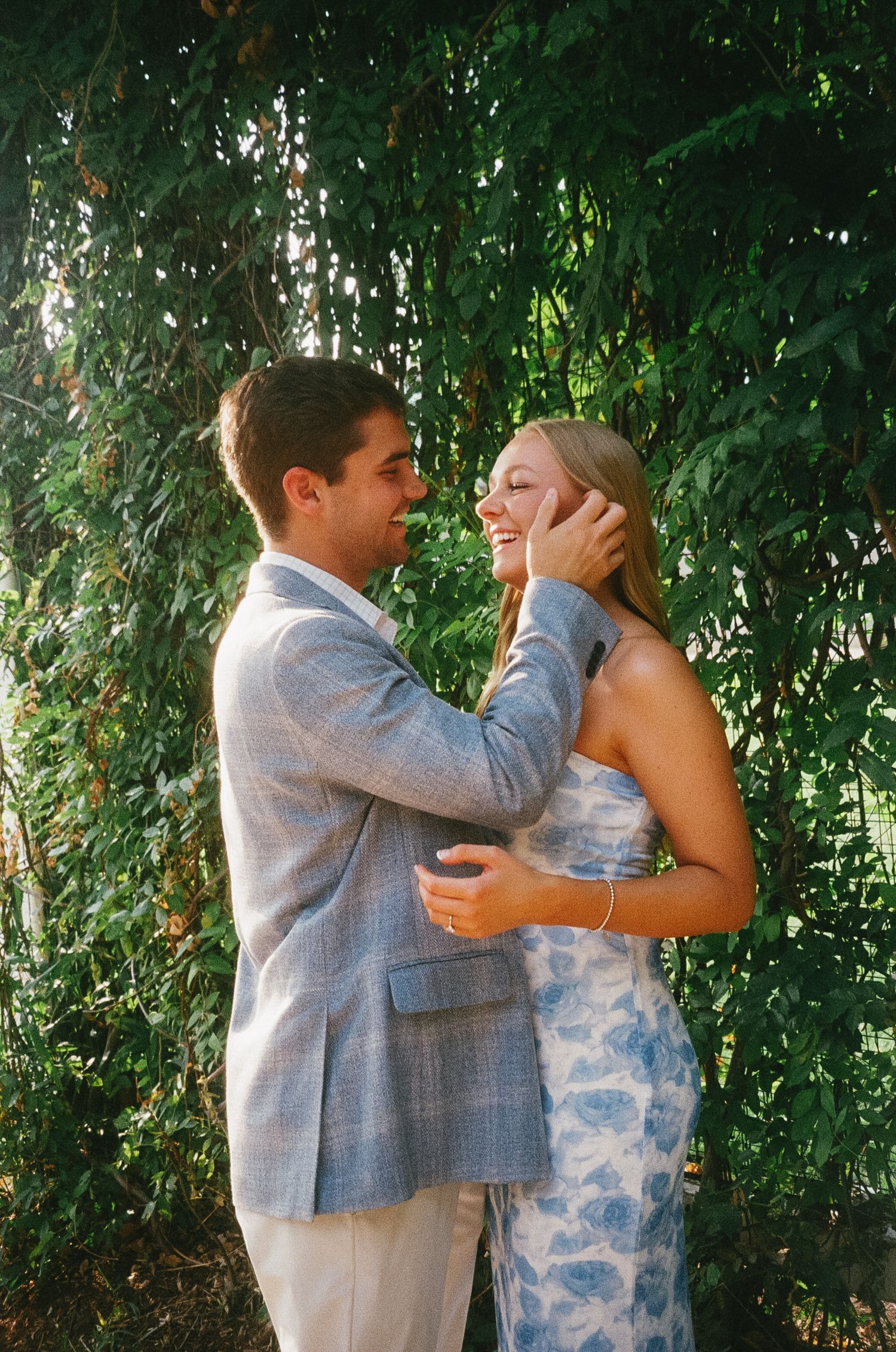 A couple shares a joyful moment together in front of lush green foliage.