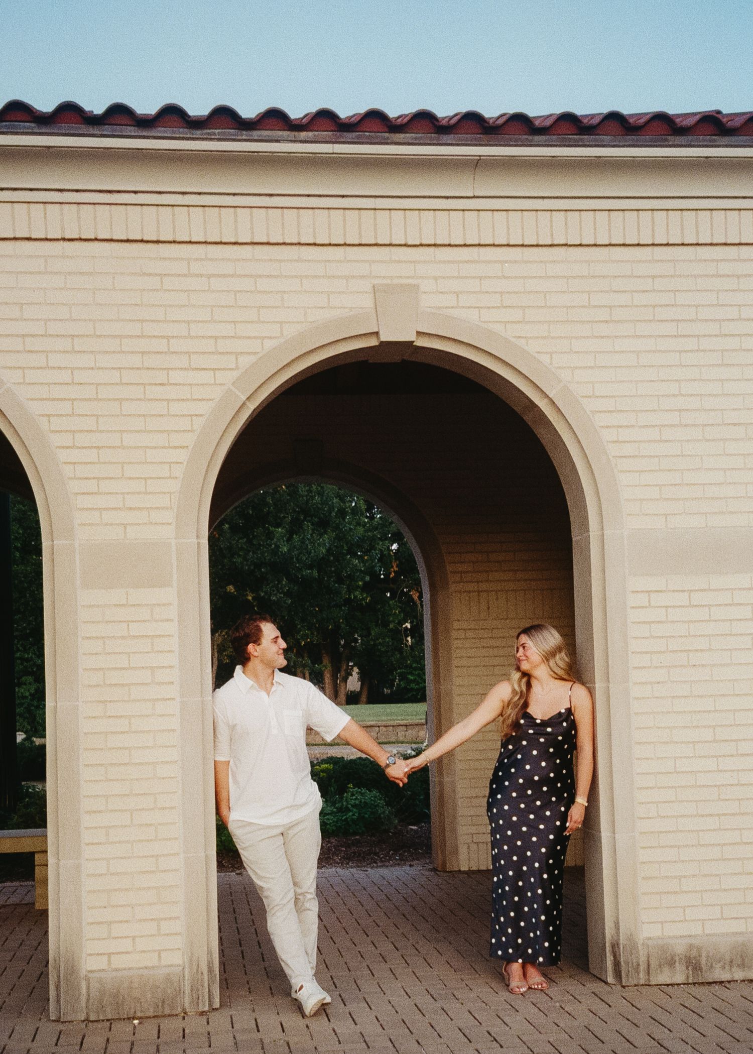 Two people playfully interact in a series of photos under cream-colored archways at a building entrance.