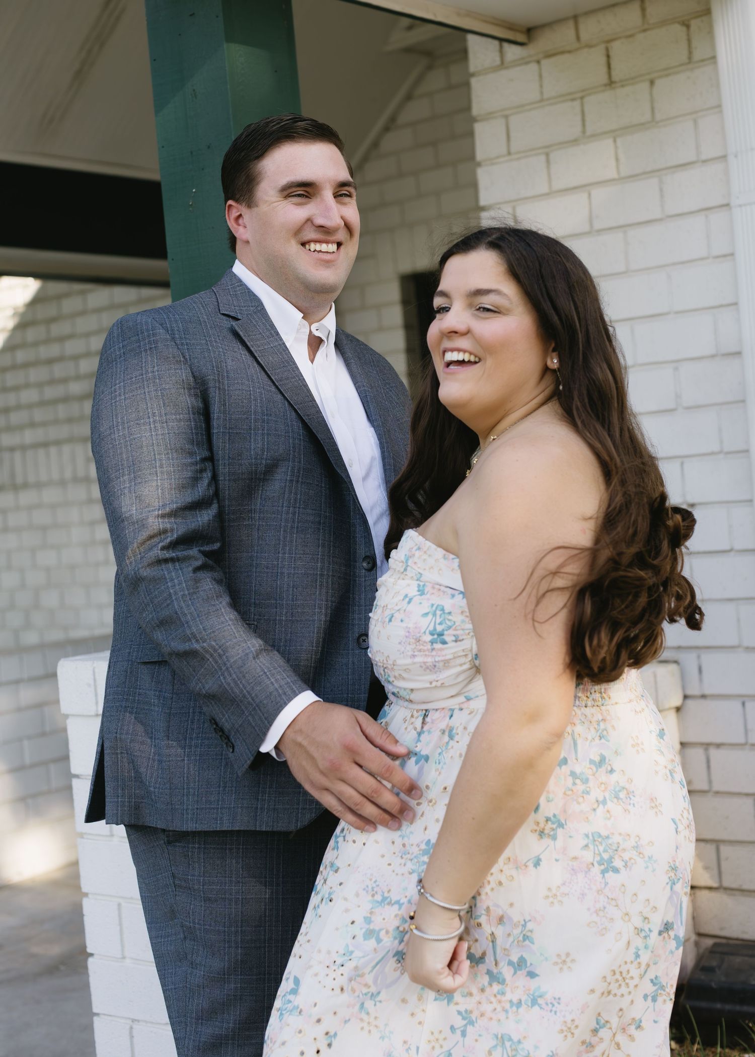 Candid moments of joy captured between a couple leaning against a white brick wall.