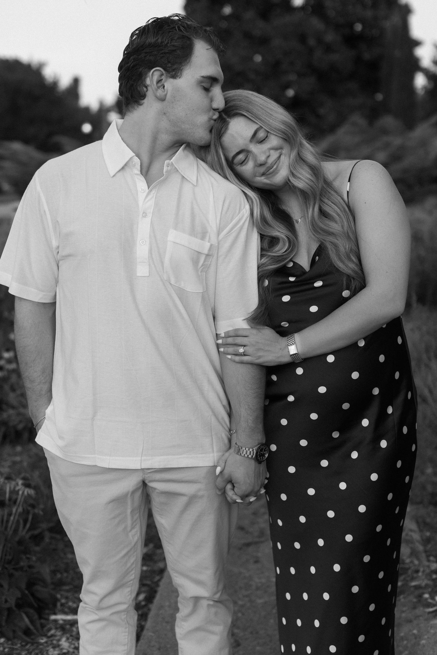 A romantic black and white photo series of a couple embracing outdoors while wearing coordinating white and polka dot outfits.