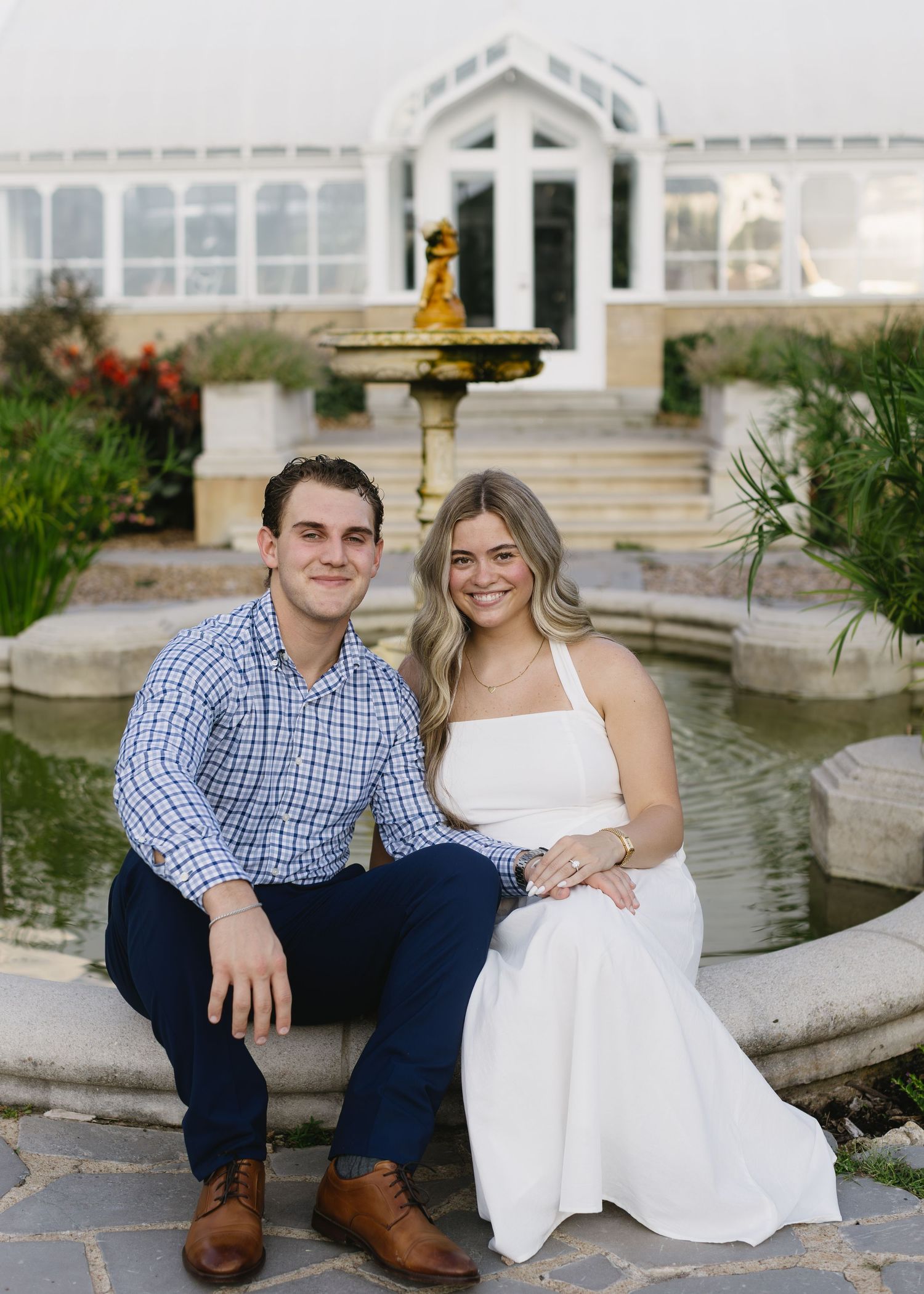 Romantic couple poses by a garden fountain in coordinated blue and white outfits.