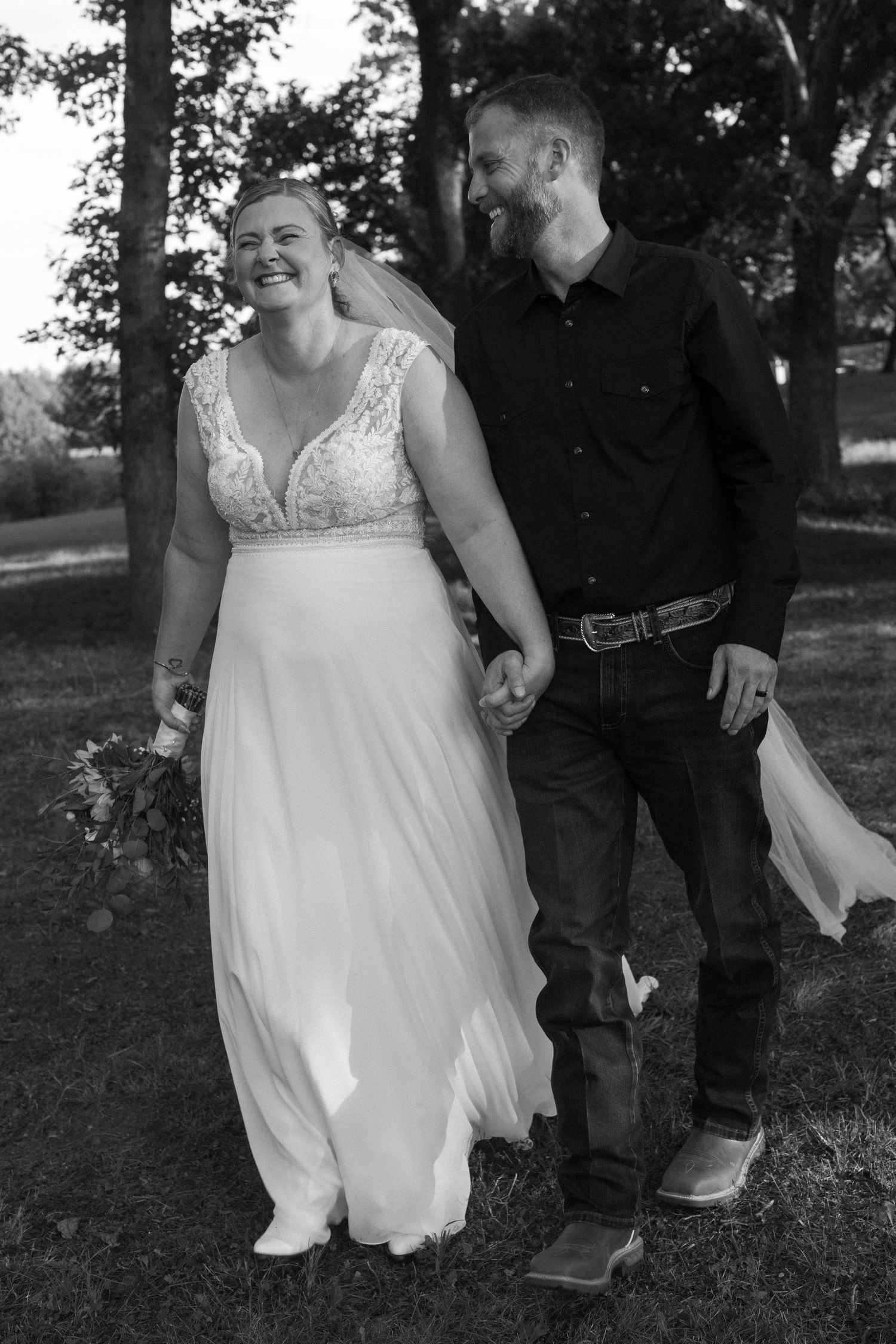 Black and white photo of a couple walking together outdoors, with the bride in a flowing white wedding dress.