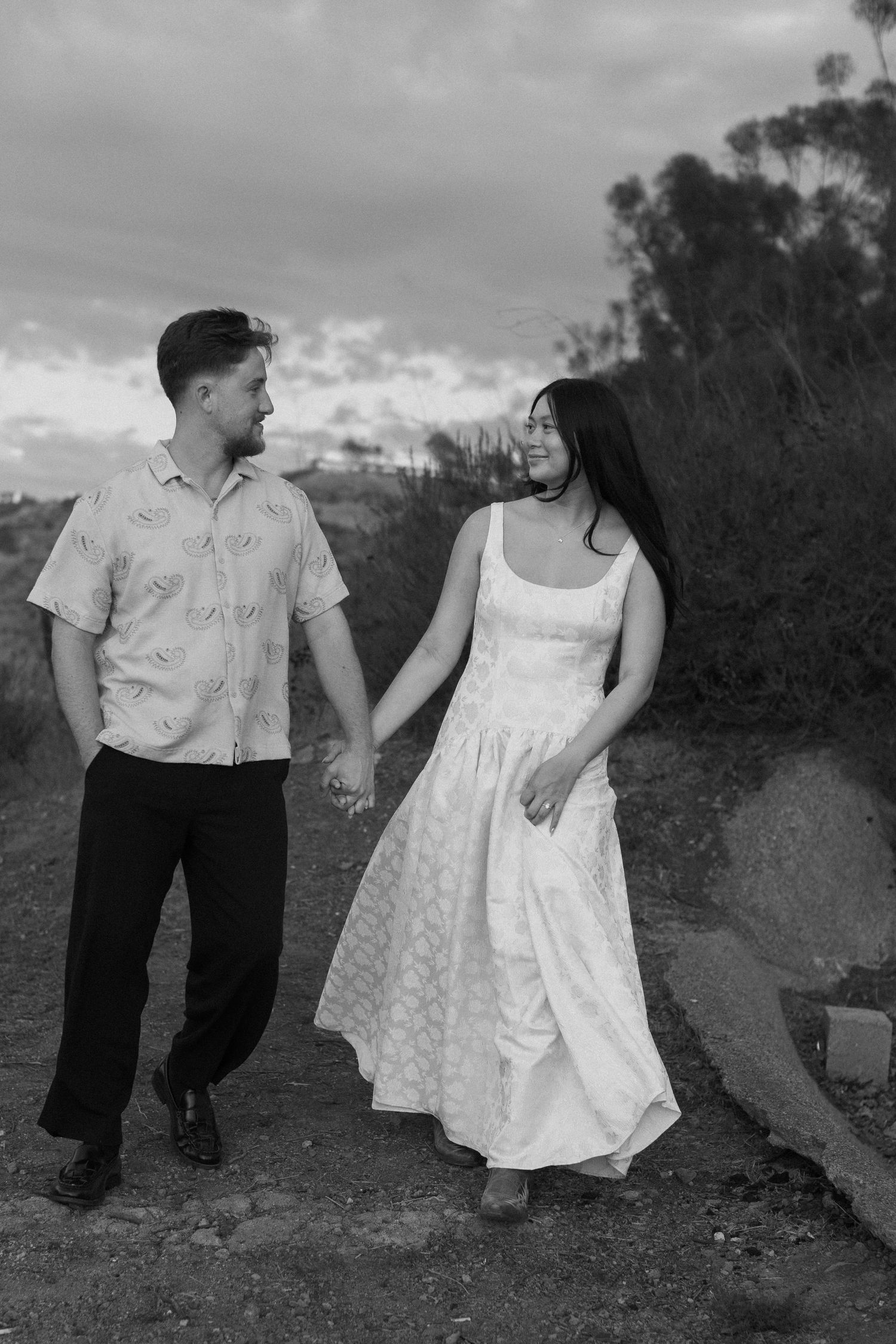 Black and white photo of couple walking together on a dirt path wearing vintage style clothing.