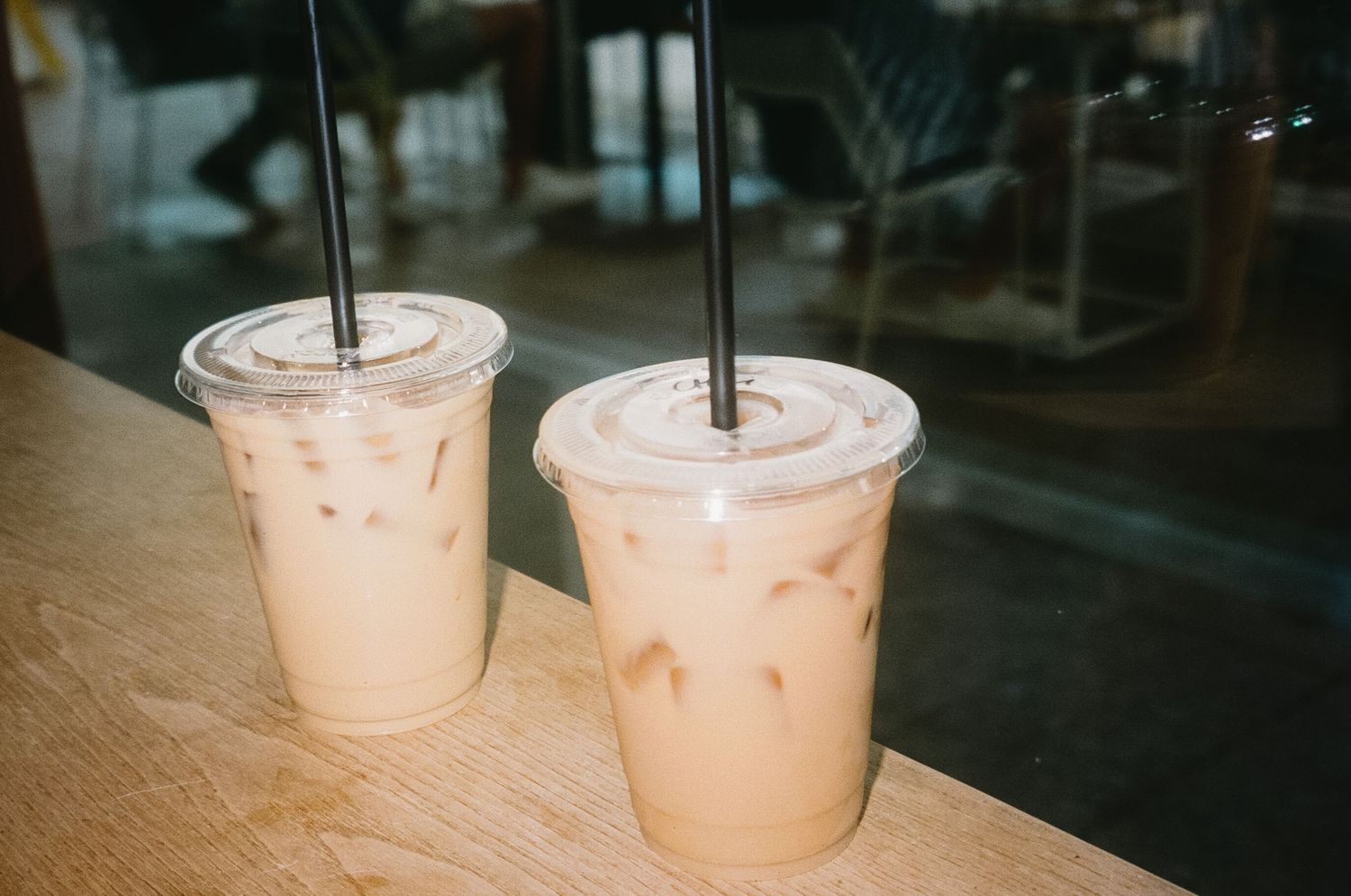Two plastic cups filled with creamy pink bubble tea beverages sit side by side on a dark surface.