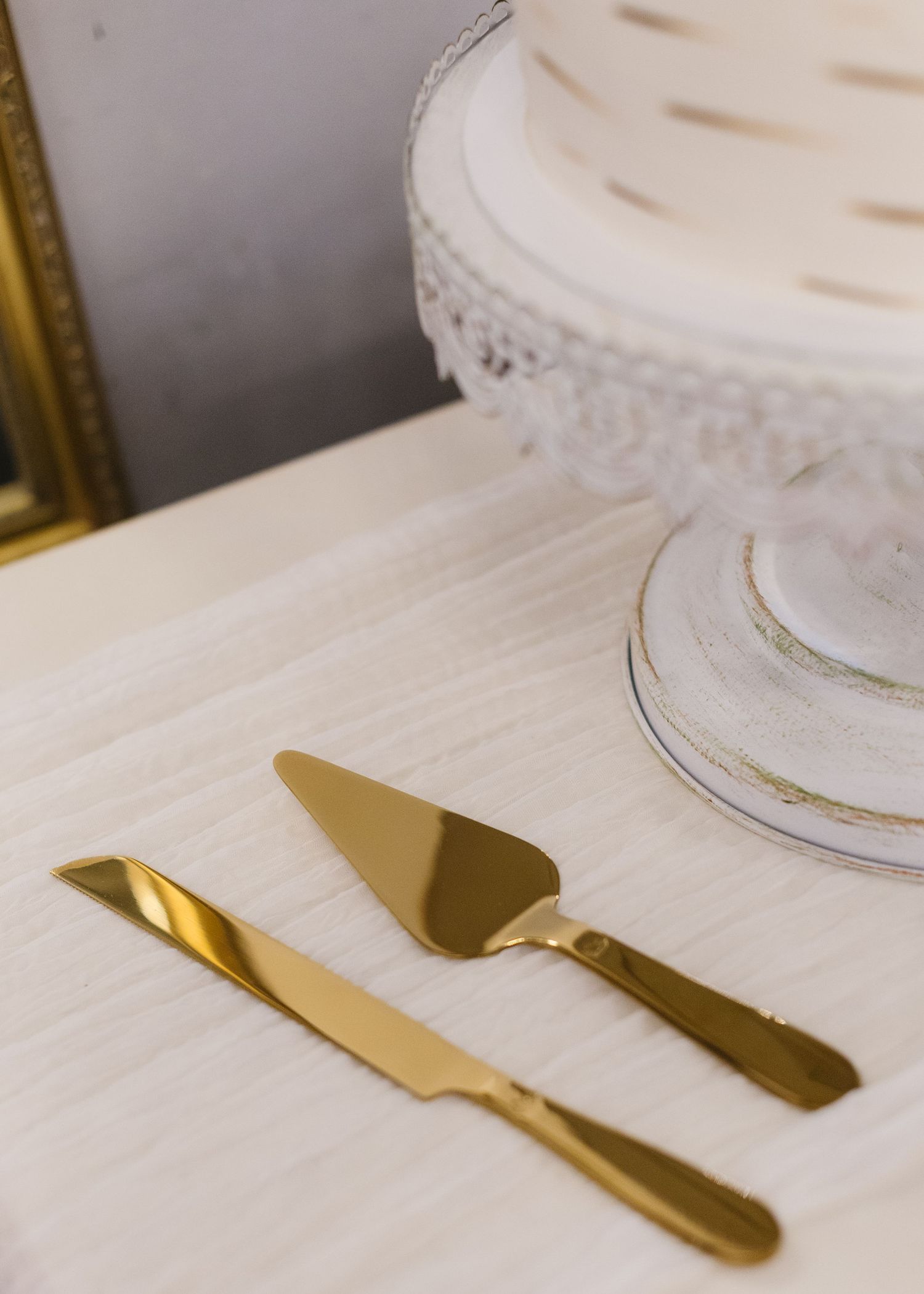 Gold cake serving utensils arranged on a white tablecloth at a wedding reception.