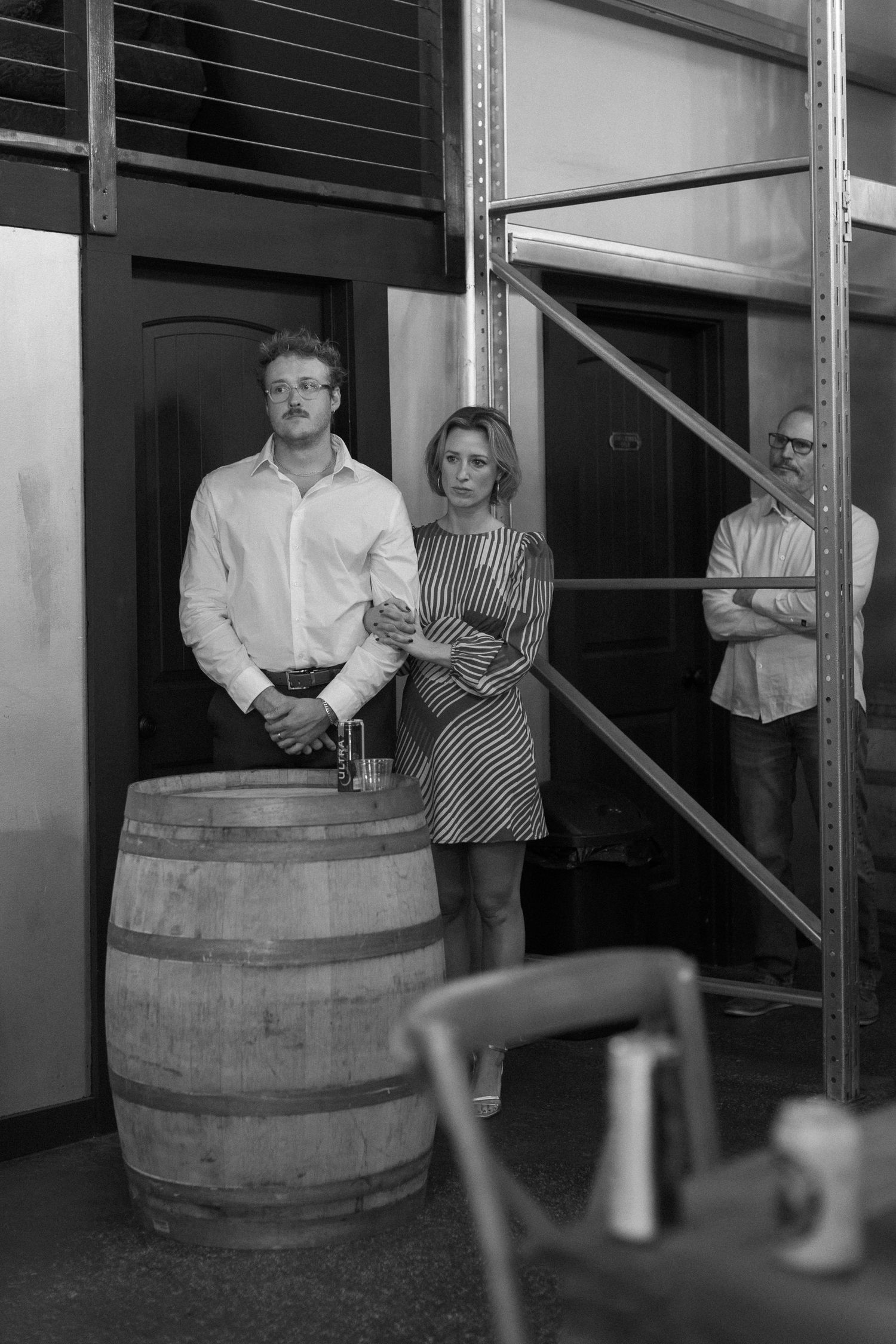 Black and white photo of people posing near wine barrels in an industrial space.