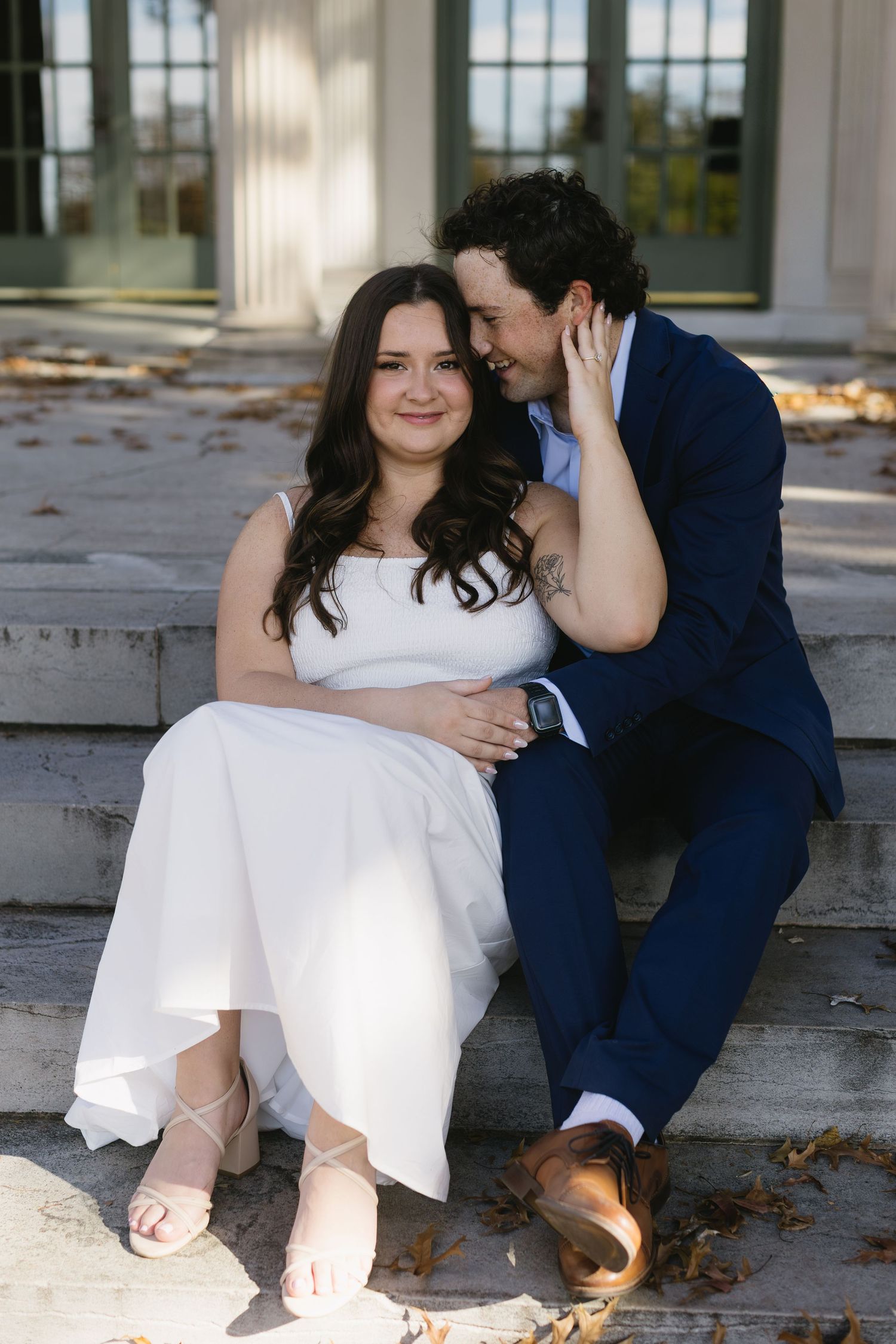 A couple sits casually on outdoor steps in formal attire during a romantic photoshoot.