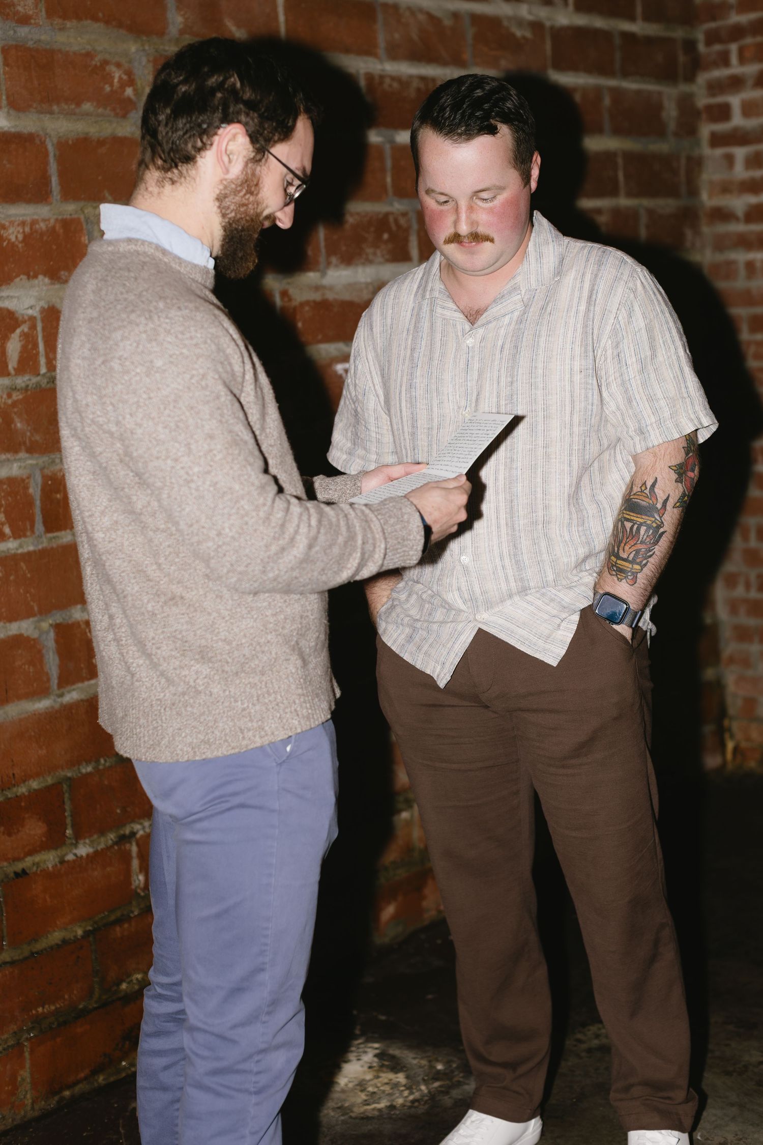 Two people reviewing paperwork together against a rustic brick wall background.