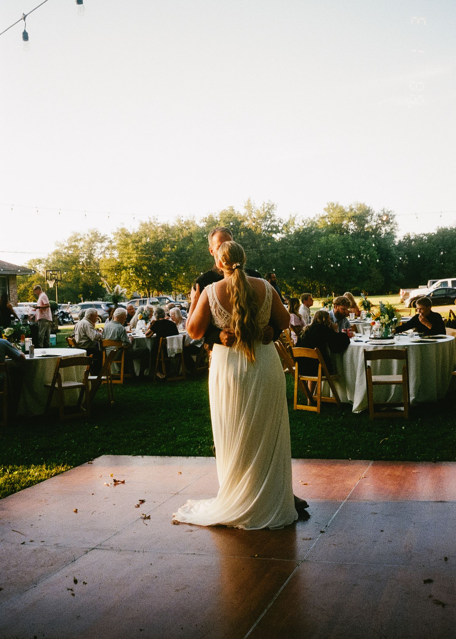 A couple shares a romantic first dance at an outdoor wedding reception during golden hour.