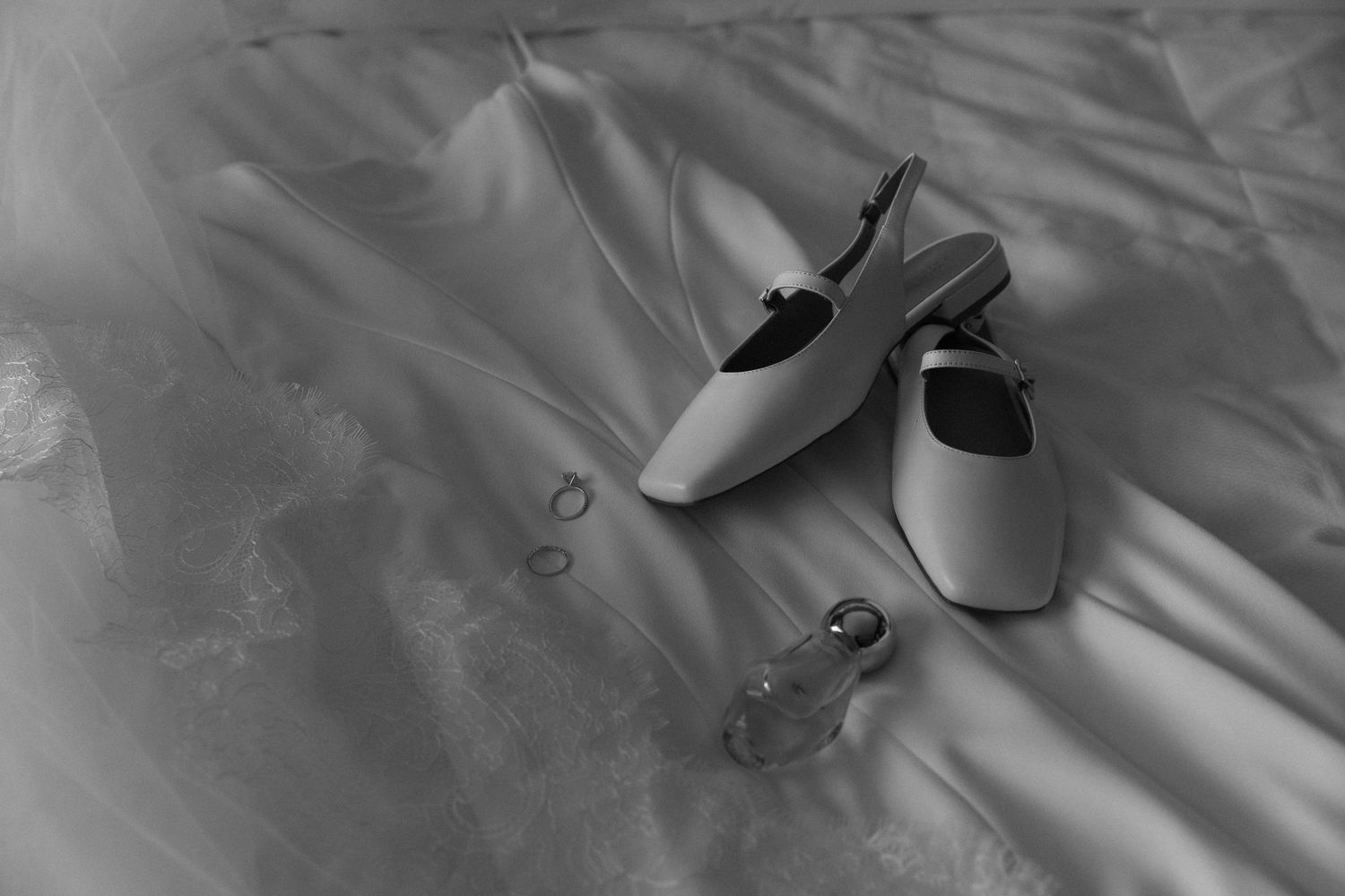 Black and white photo showing the flowing fabric of a wedding dress against bedding.