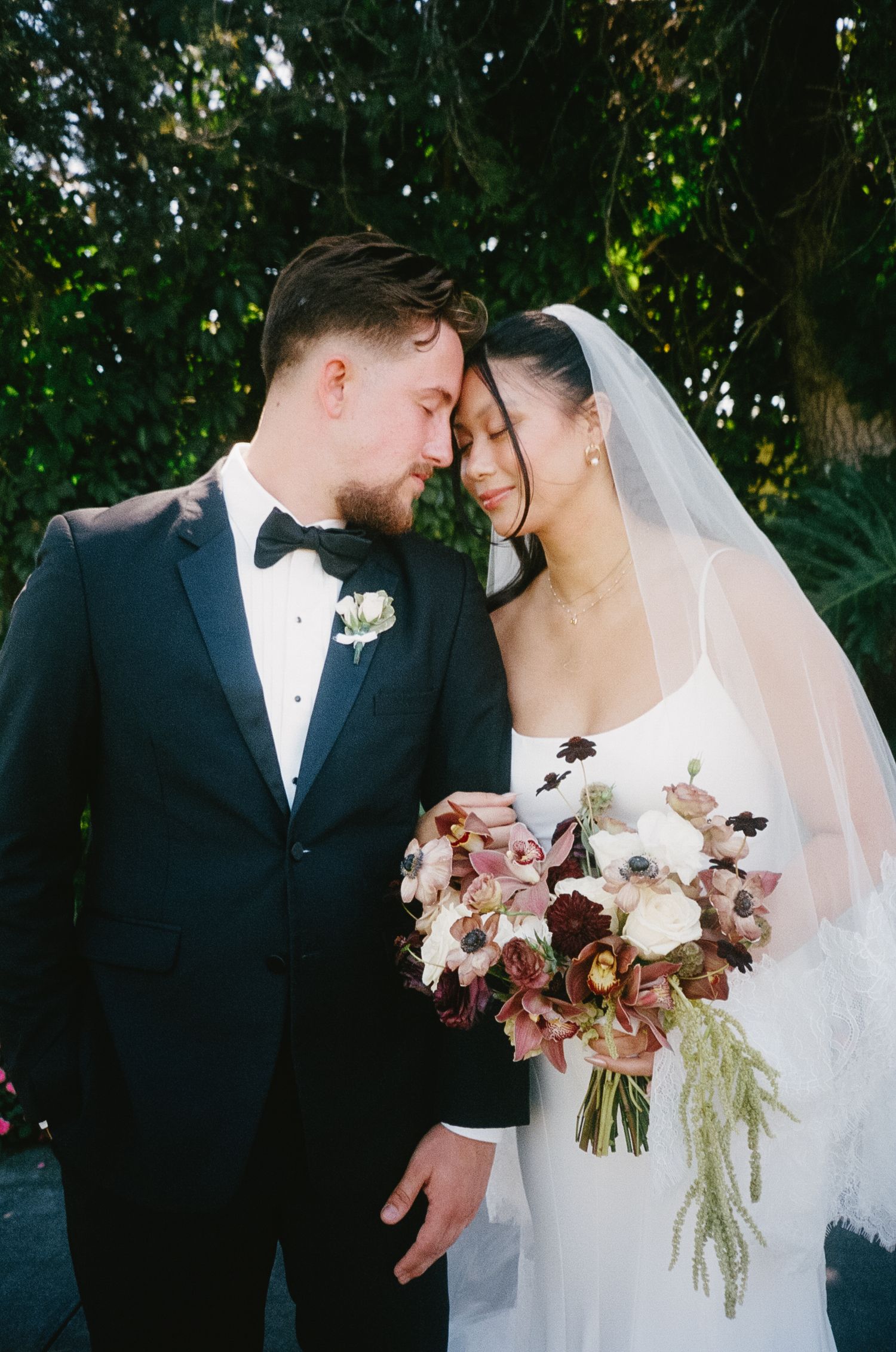 Romantic wedding couple sharing an intimate moment outdoors with a beautiful floral bouquet.