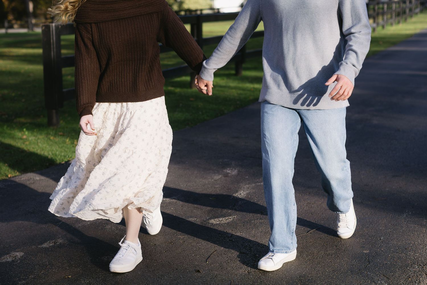 Close-up view of white sneakers and dress shoes walking together on a paved pathway in an outdoor setting.