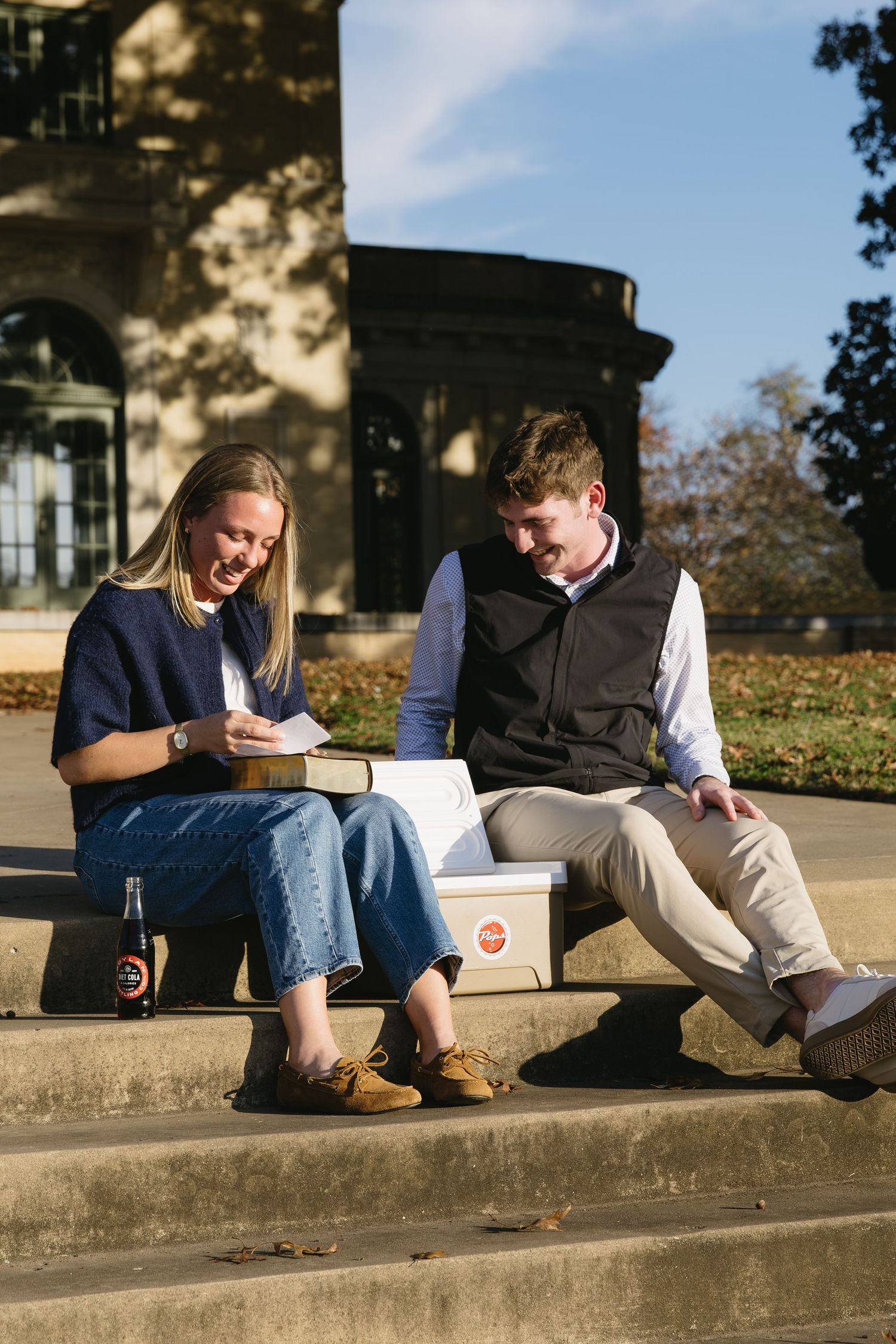 Couple sitting on concrete steps outdoors on a sunny autumn day sharing a relaxed moment.