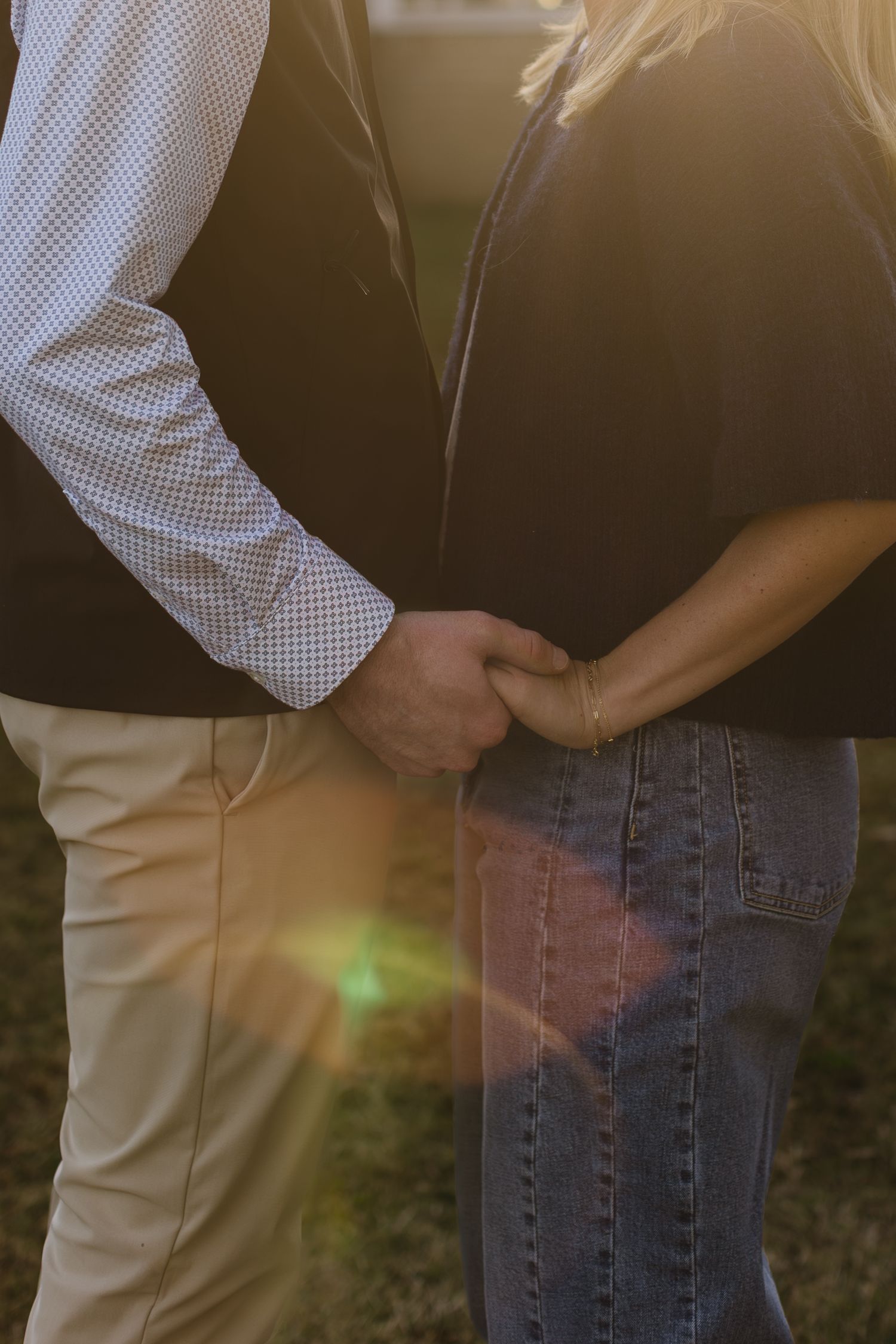 Intimate close-up shot of a couple holding hands in casual clothing at sunset.