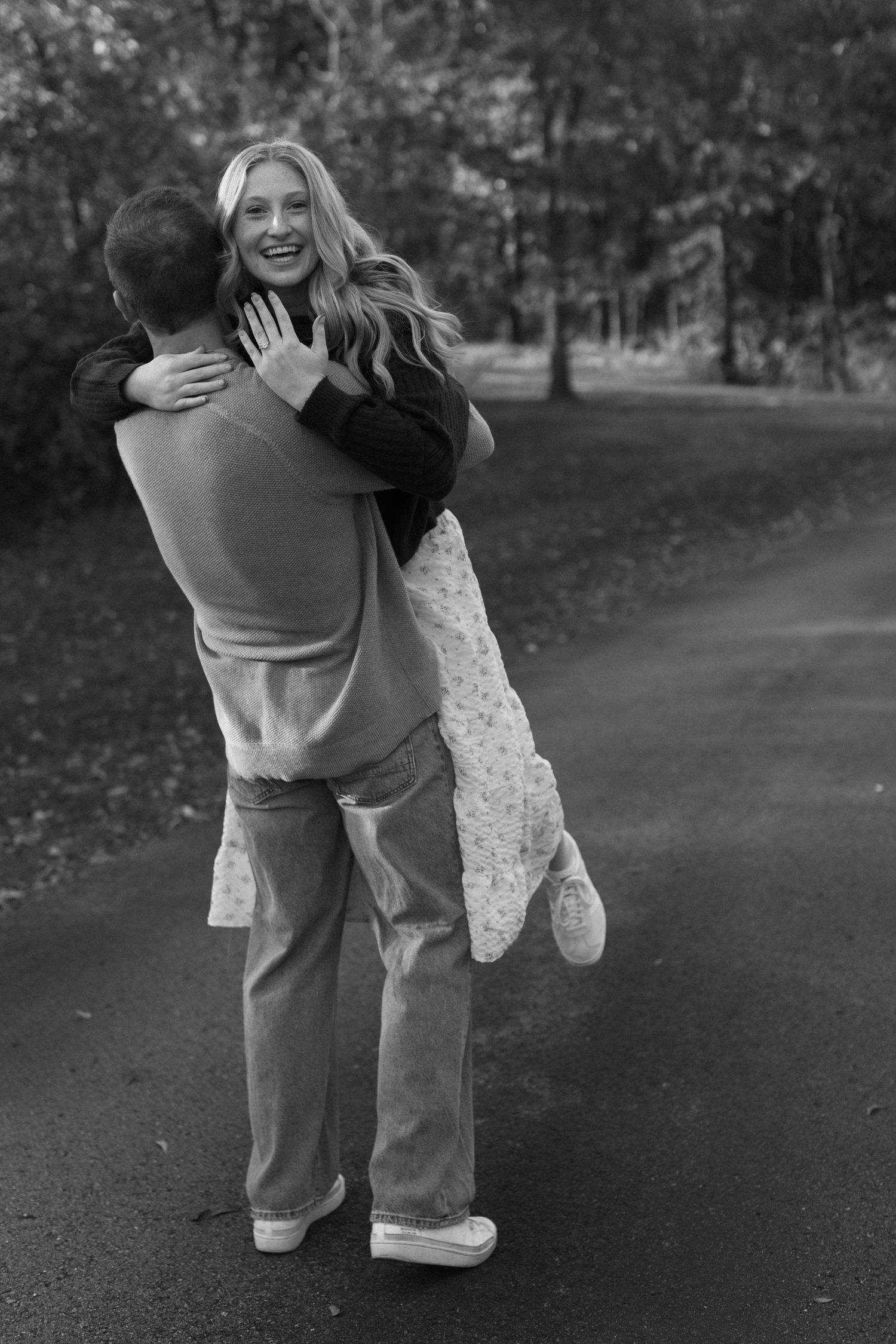 A couple sharing a joyful dance moment on a park path in black and white.