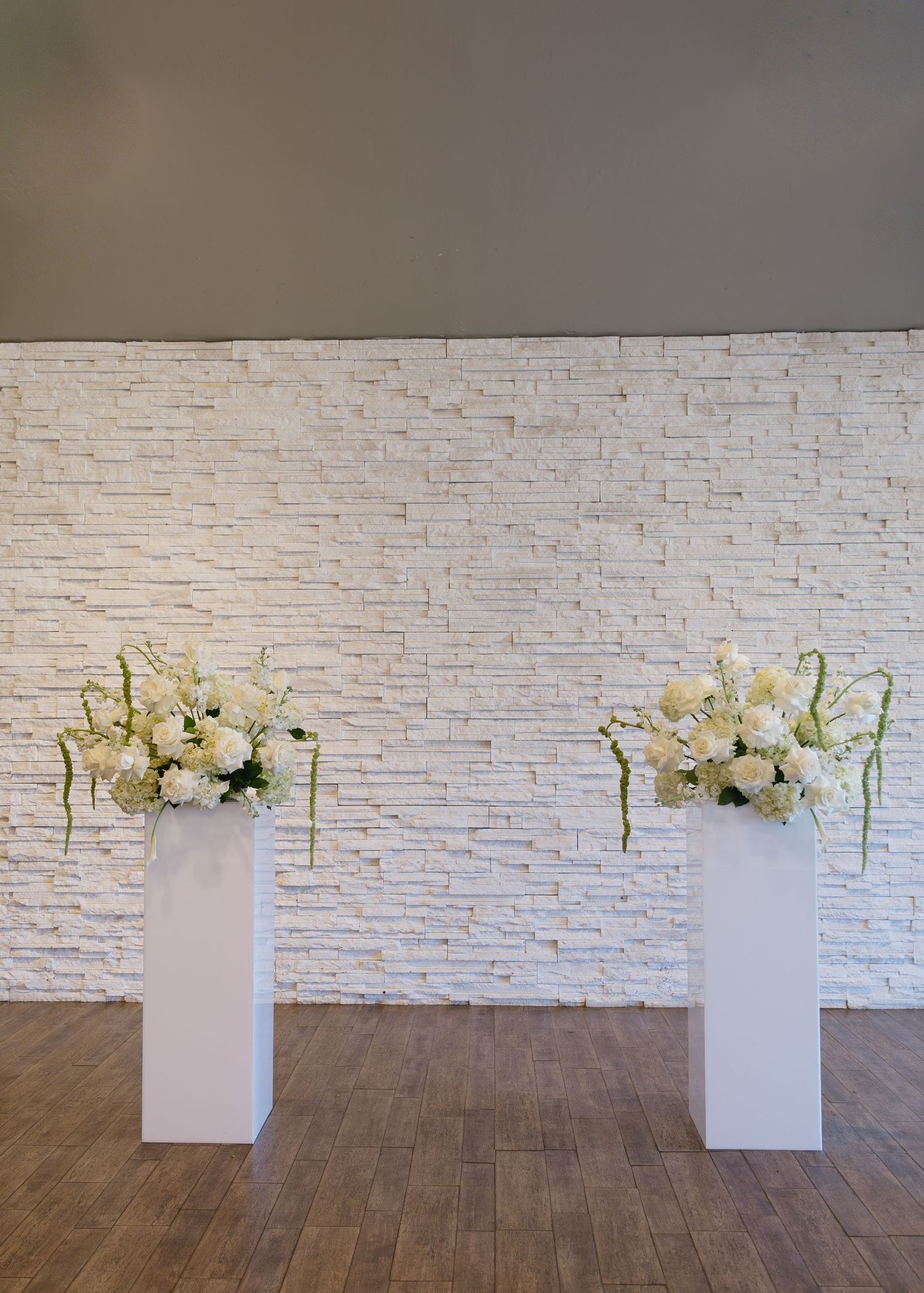 White floral arrangements on pedestals against a textured brick wall.