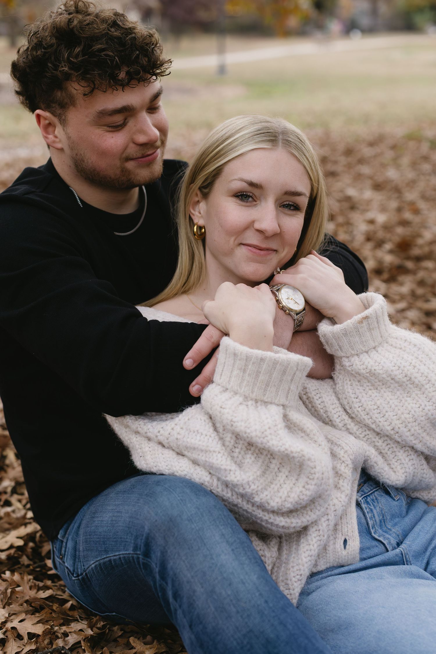 A romantic fall portrait of a couple sitting on fallen leaves wearing coordinated casual outfits.