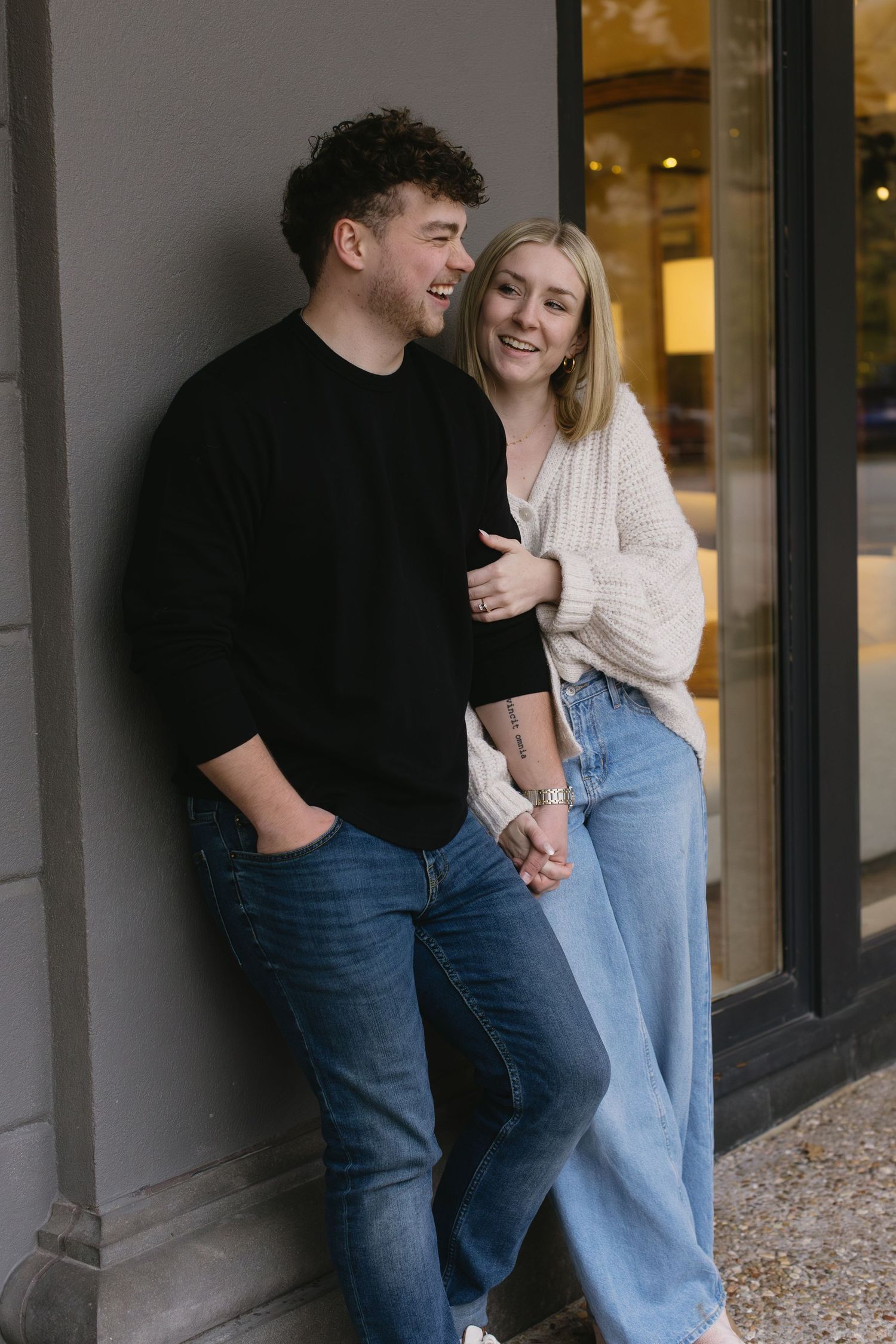A couple shares a lighthearted moment while leaning against a building exterior.