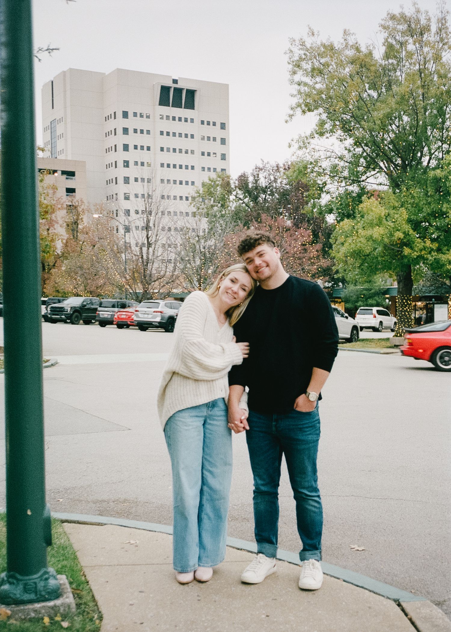 Couple in casual wear sharing playful moments between green poles in a parking lot.