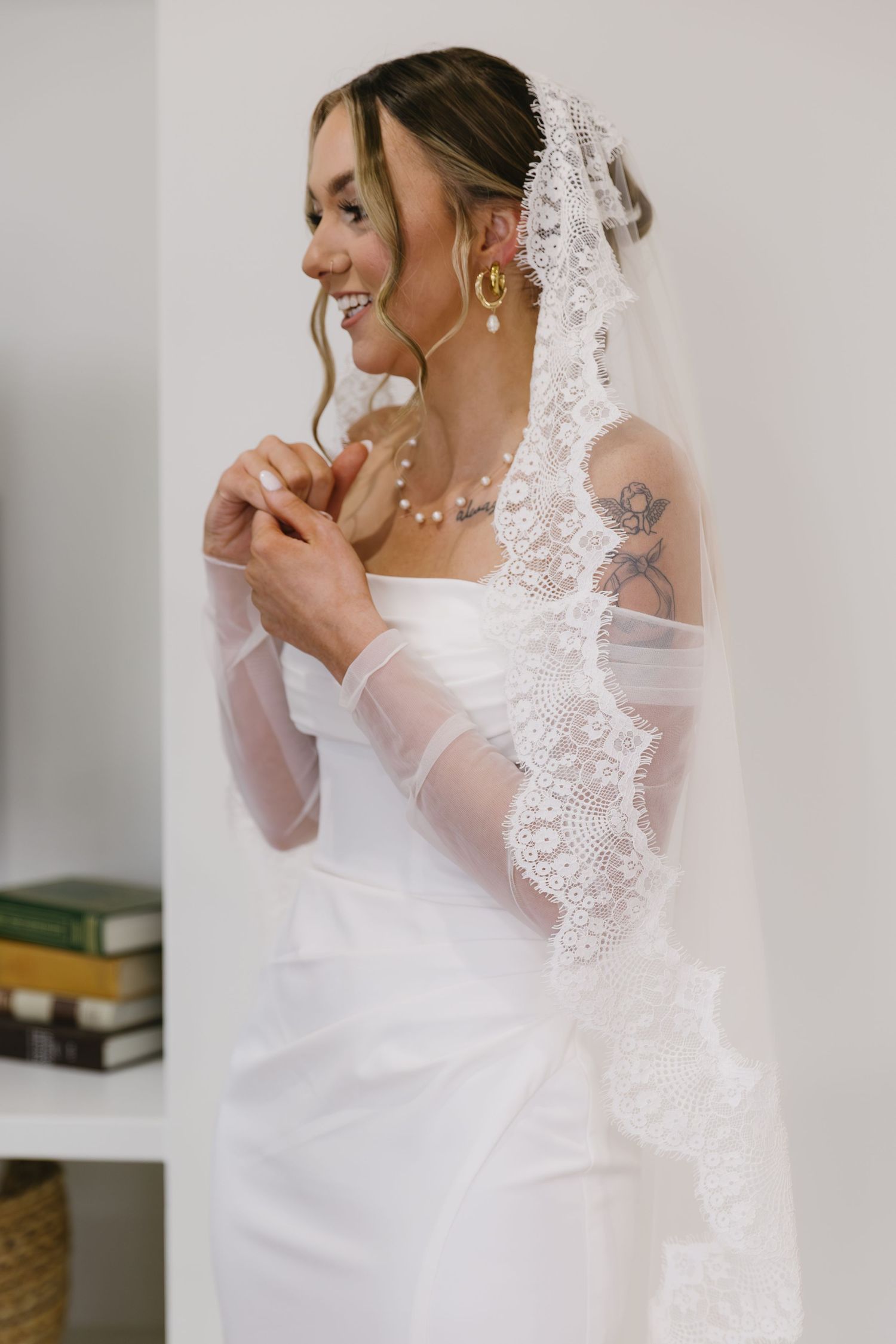 Bride in elegant lace veil and white dress smiling while getting ready.