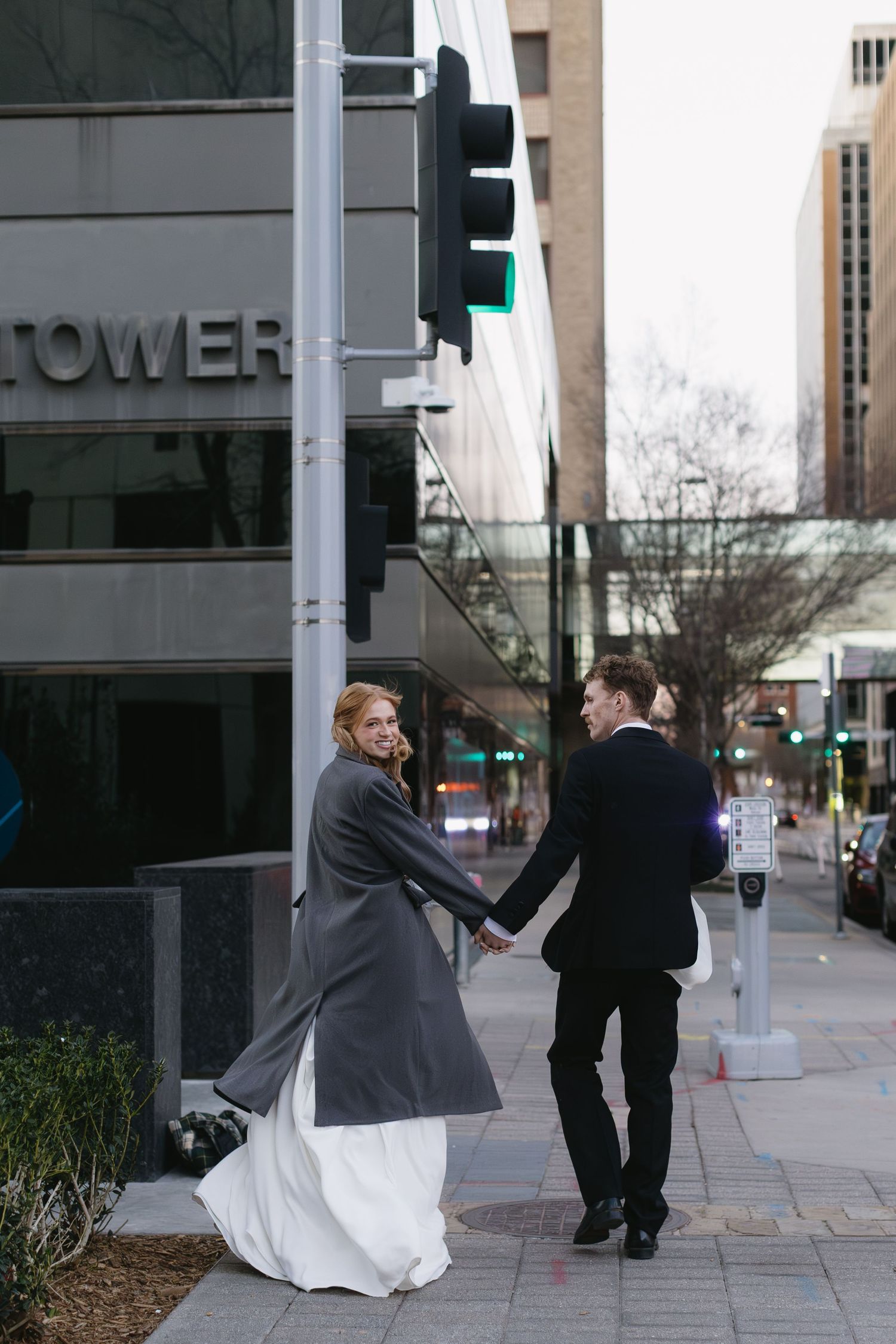 Wedding couple dances playfully on urban sidewalk near modern buildings.