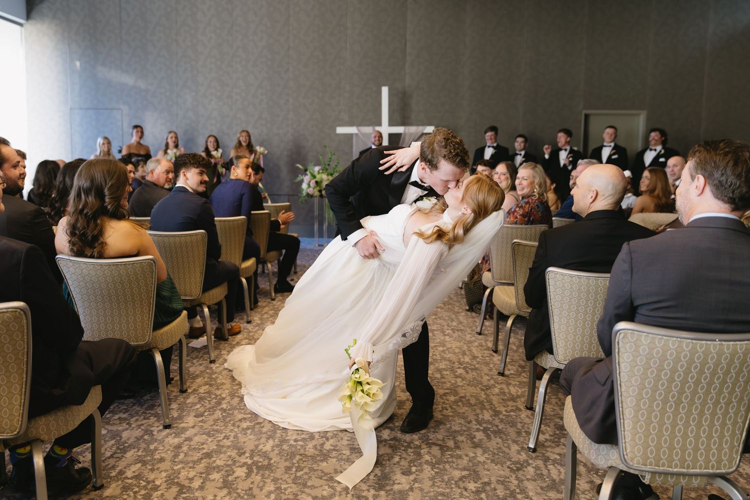 Wedding reception scene with guests seated at round tables in an elegant ballroom.