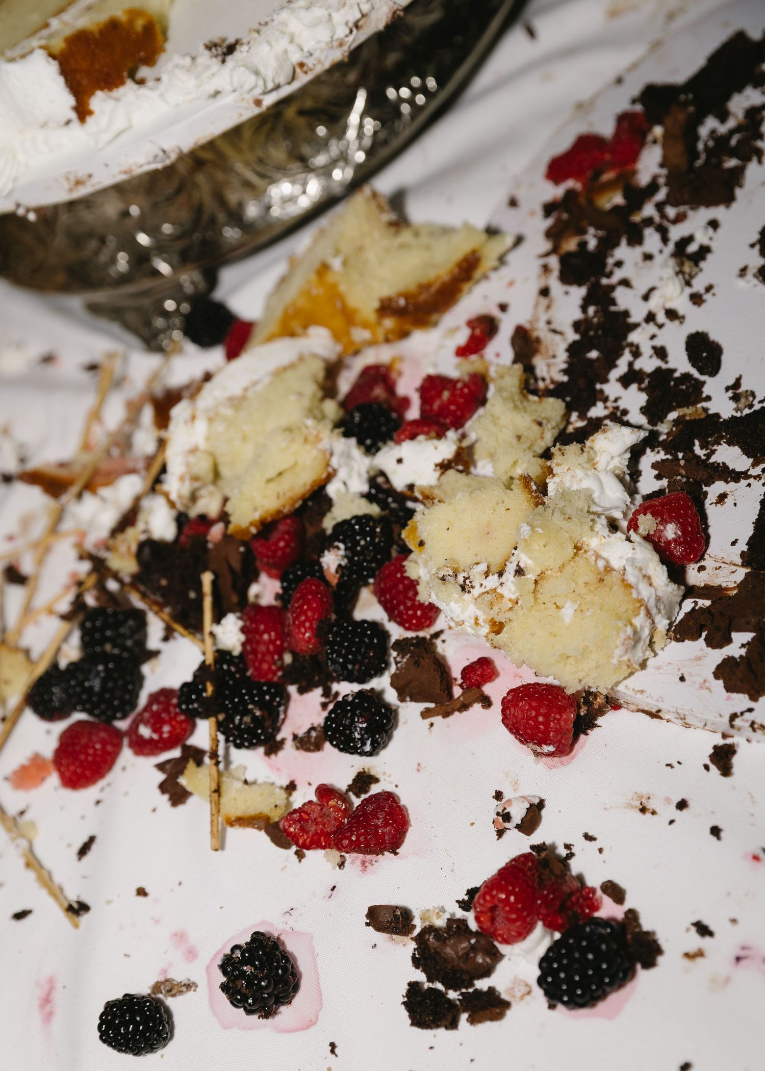 Scattered berries and cake crumbs on white surface creating artistic dessert presentation.