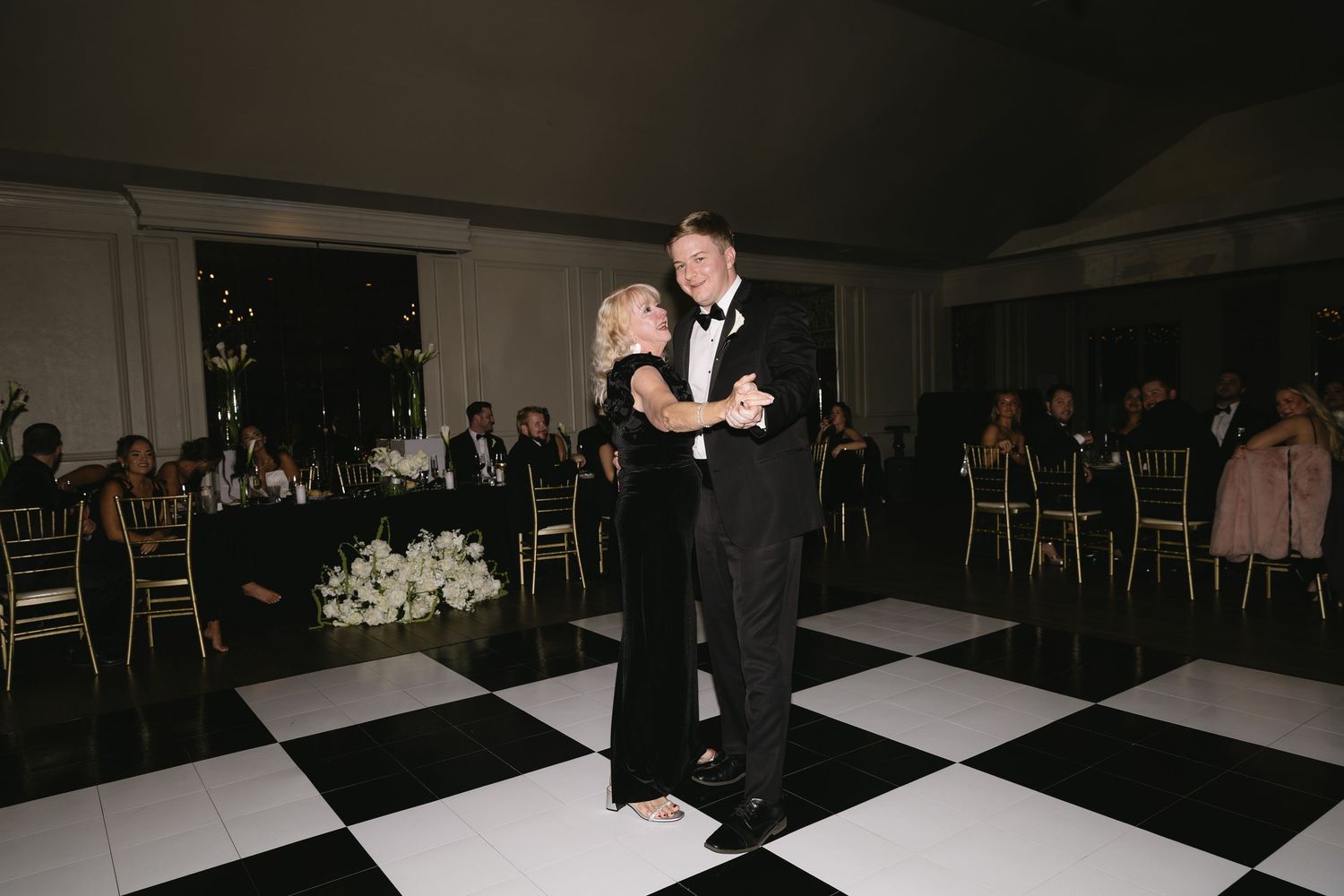 A dimly lit wedding reception venue with guests gathered on the dance floor.