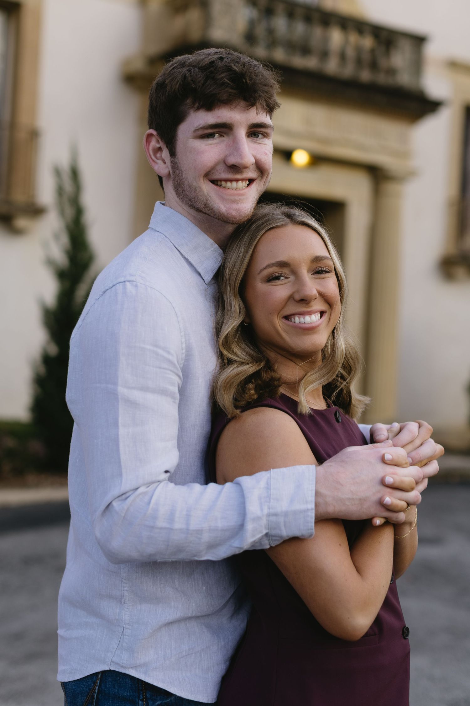 A happy couple embraces while posing for a casual portrait outdoors.