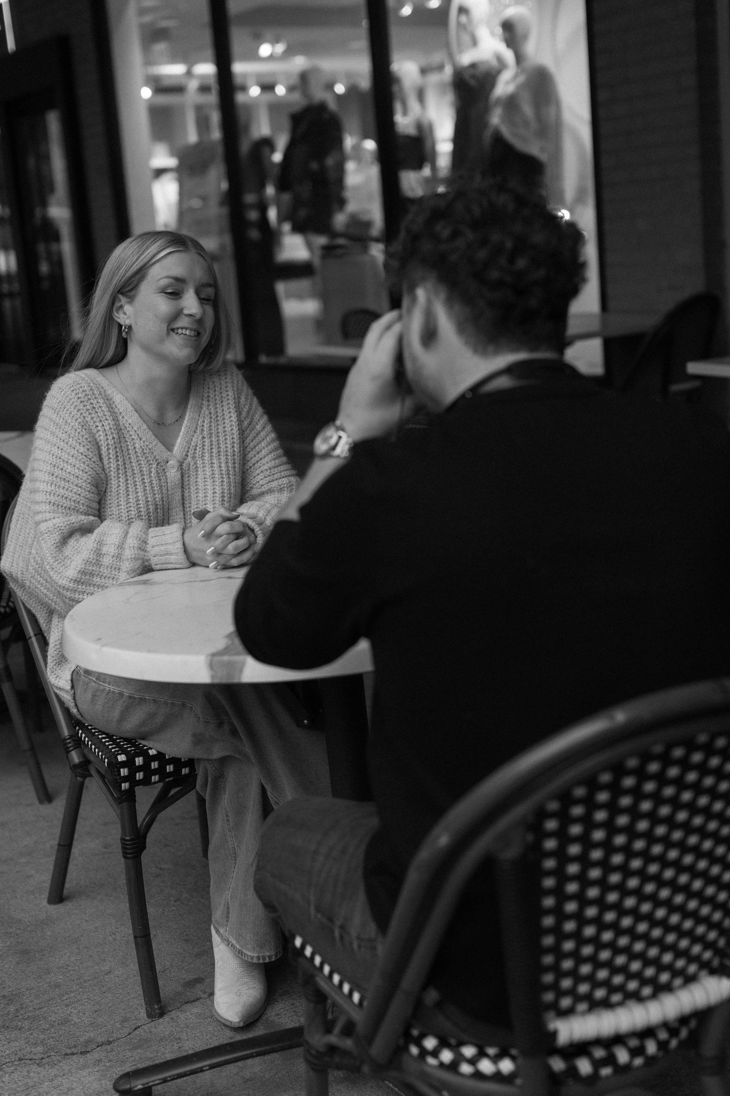 A black and white photo of a couple sharing a moment at an outdoor cafe table.