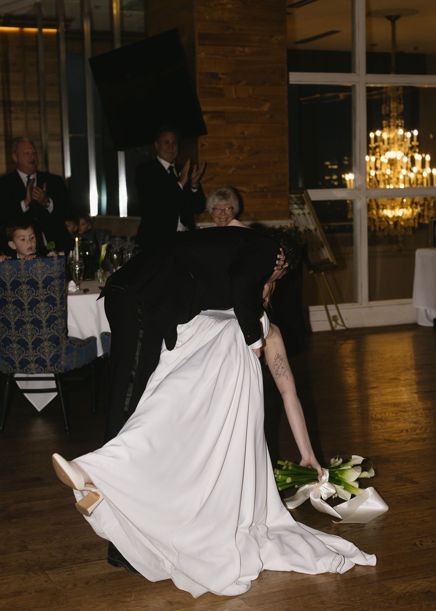 Wedding couple performs romantic dance on wooden floor under chandelier lighting.