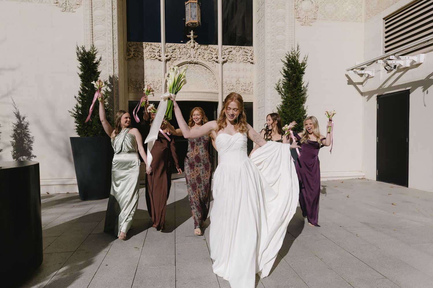 Wedding party walking outside modern building with architectural details and potted plants.