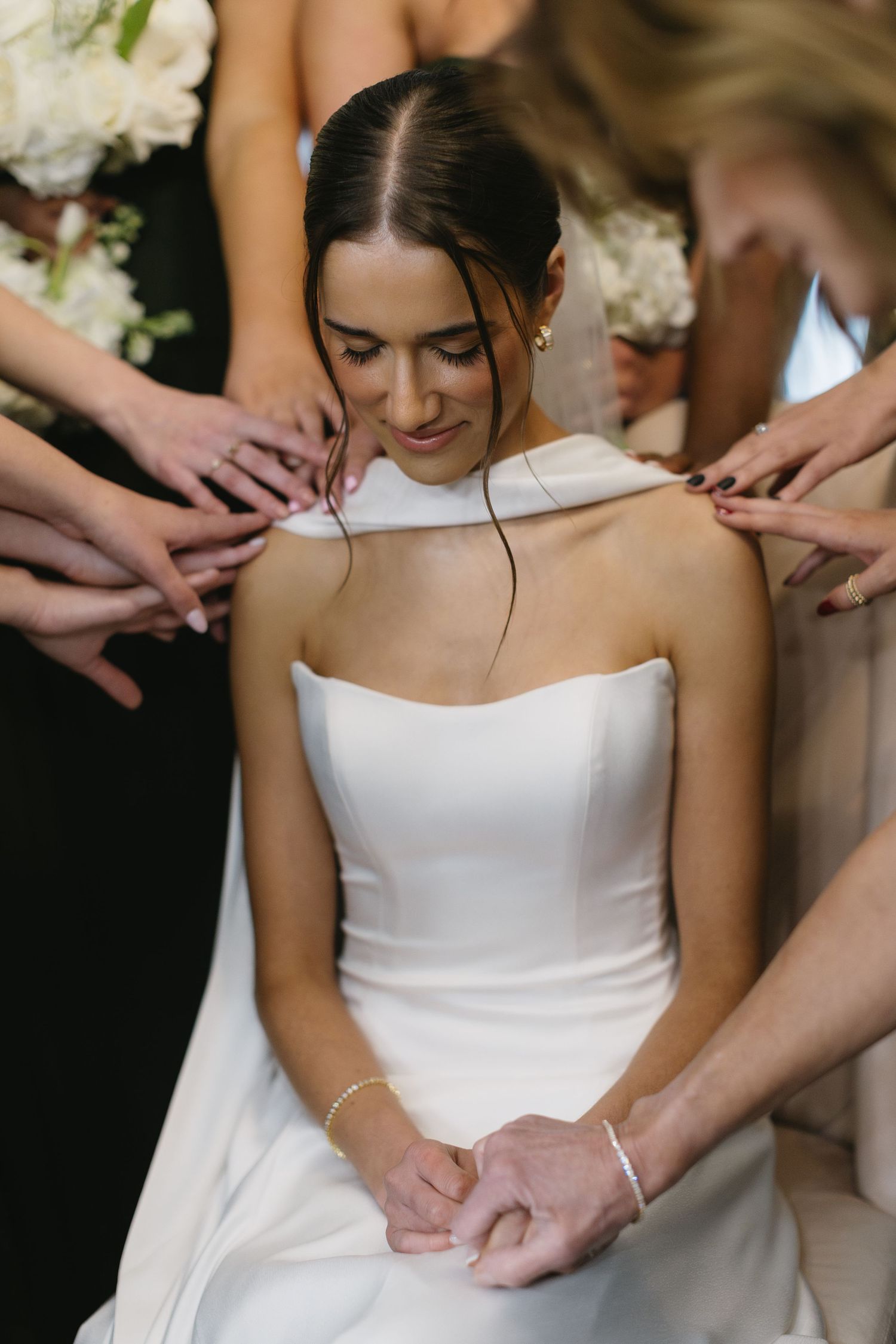 Hands helping to adjust and button up the back of an elegant white wedding dress.