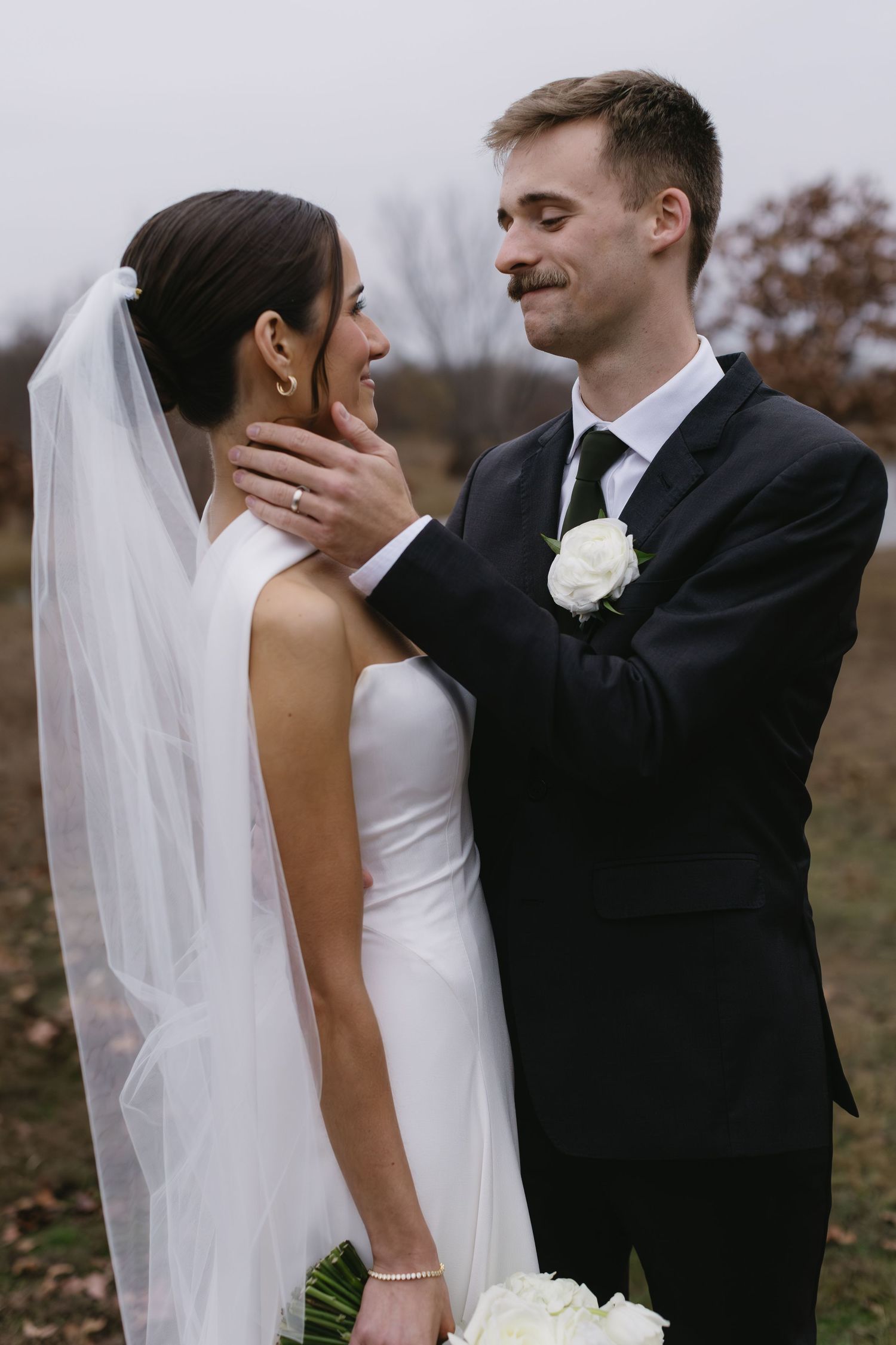 Bride in white dress and groom in black suit share intimate moments during outdoor wedding photos.