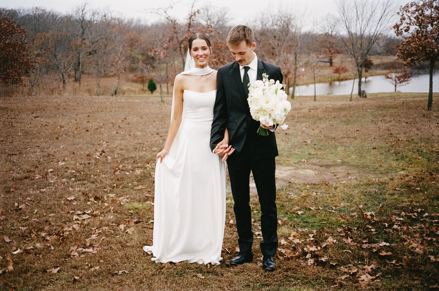 Outdoor wedding portraits taken in a rustic fall setting with brown grass and bare trees.