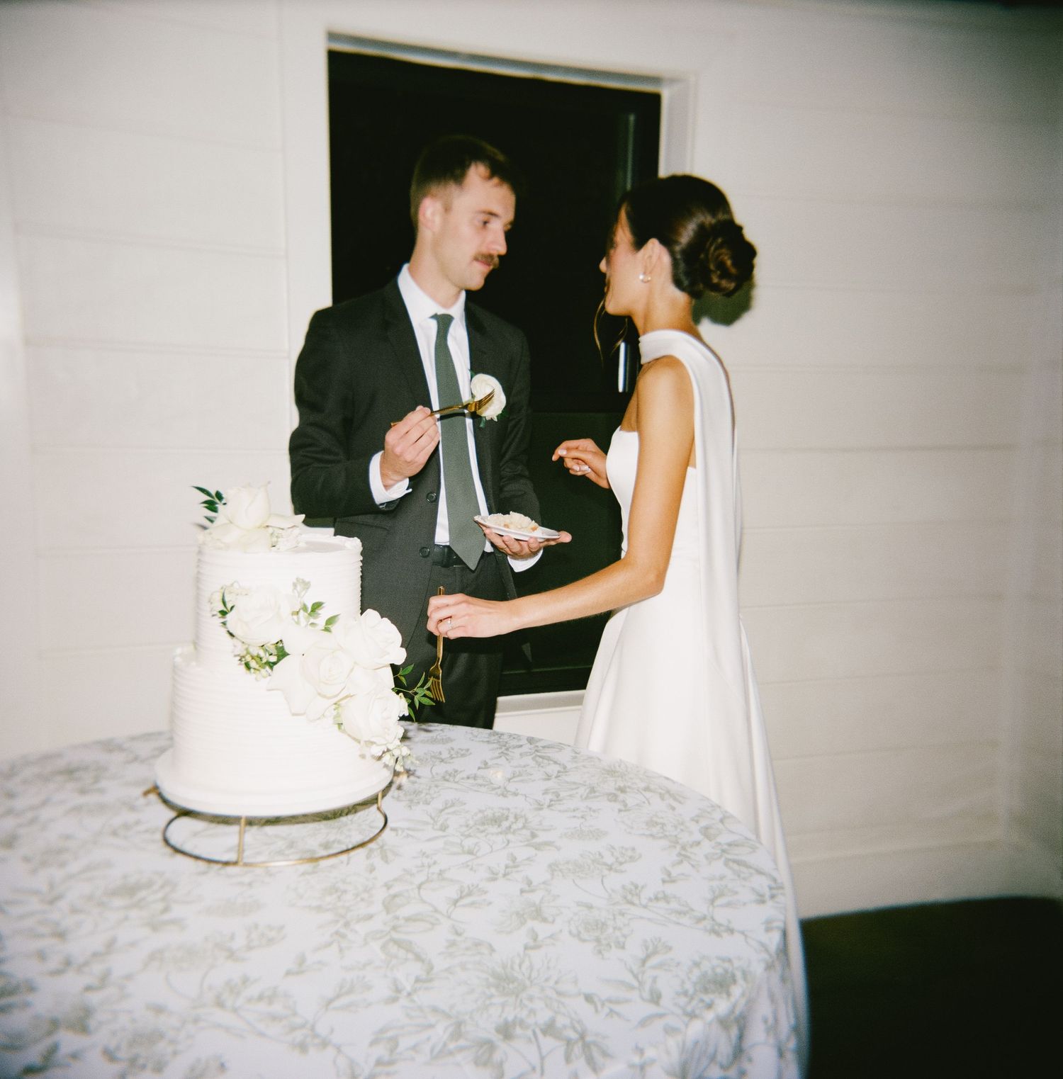 Couple shares a moment while cutting their elegant white wedding cake at the reception.