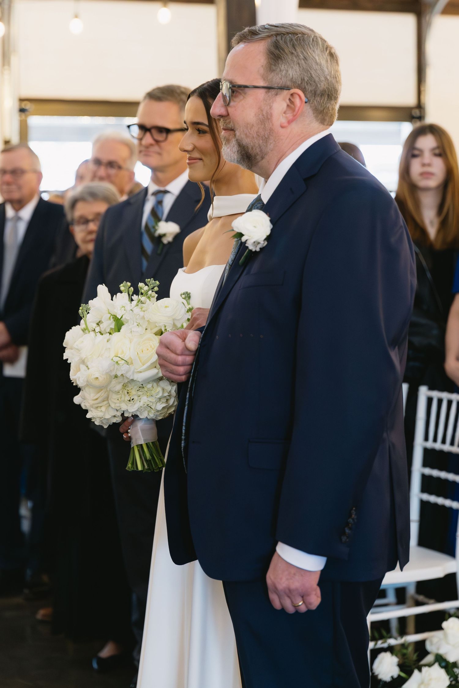 Wedding ceremony in progress with couple at altar surrounded by white floral arrangements.