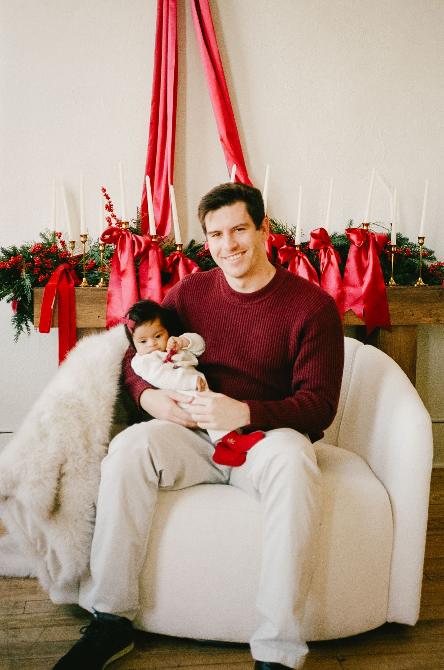 Relaxed family photoshoot on white furniture with burgundy and white holiday decor.
