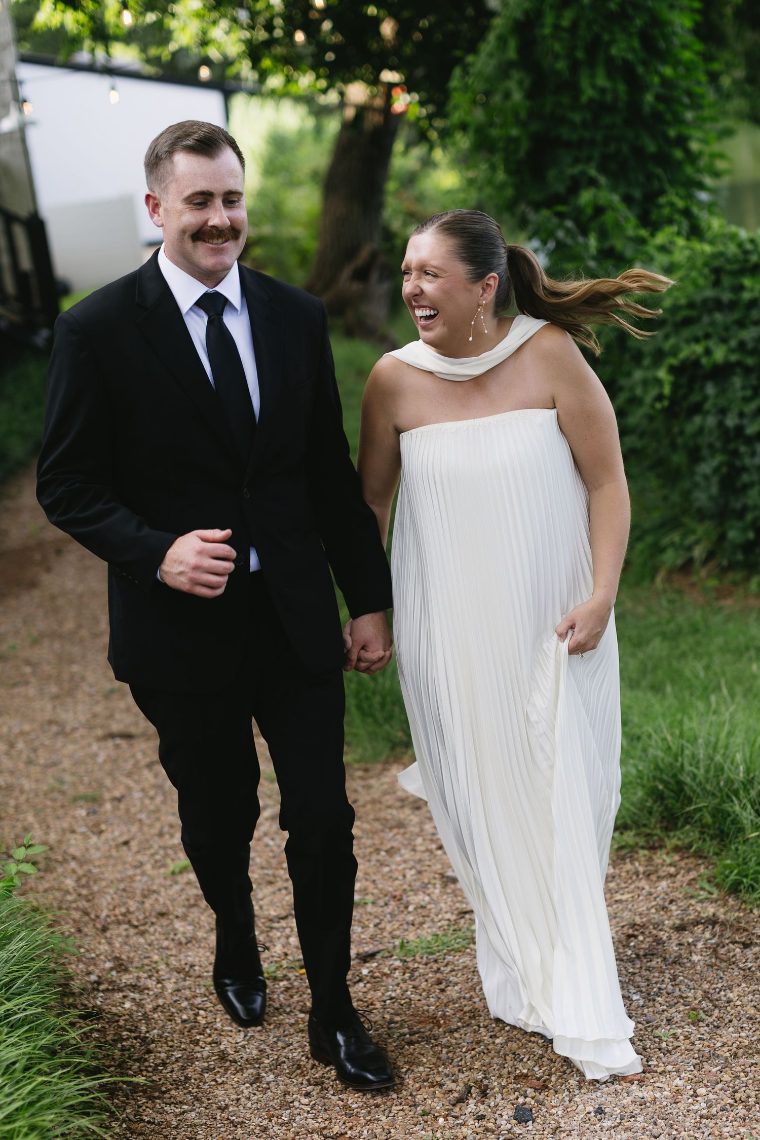 Couple walking and laughing together on a garden path during their wedding day.