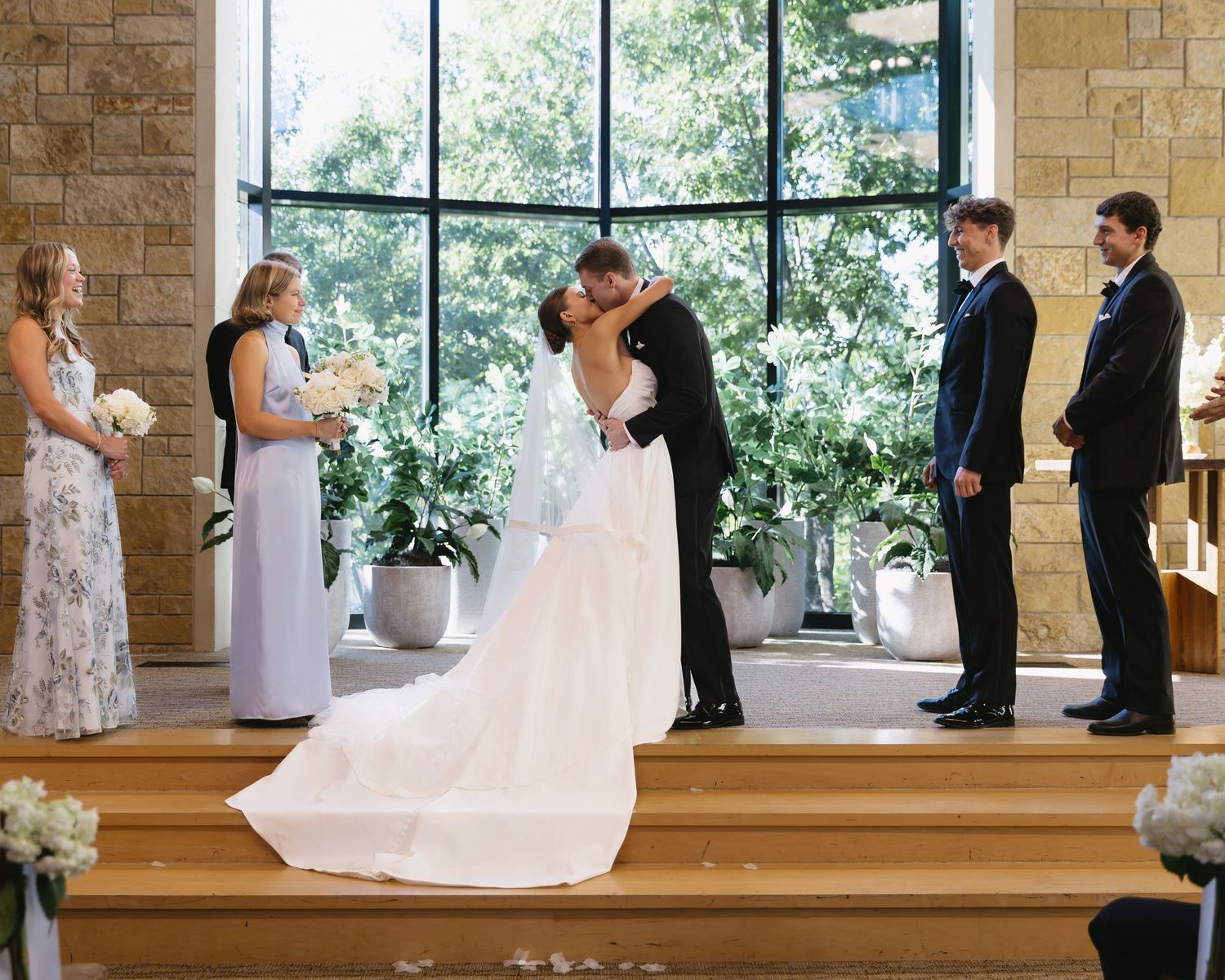 Wedding ceremony in progress at modern stone chapel with large windows and natural light.